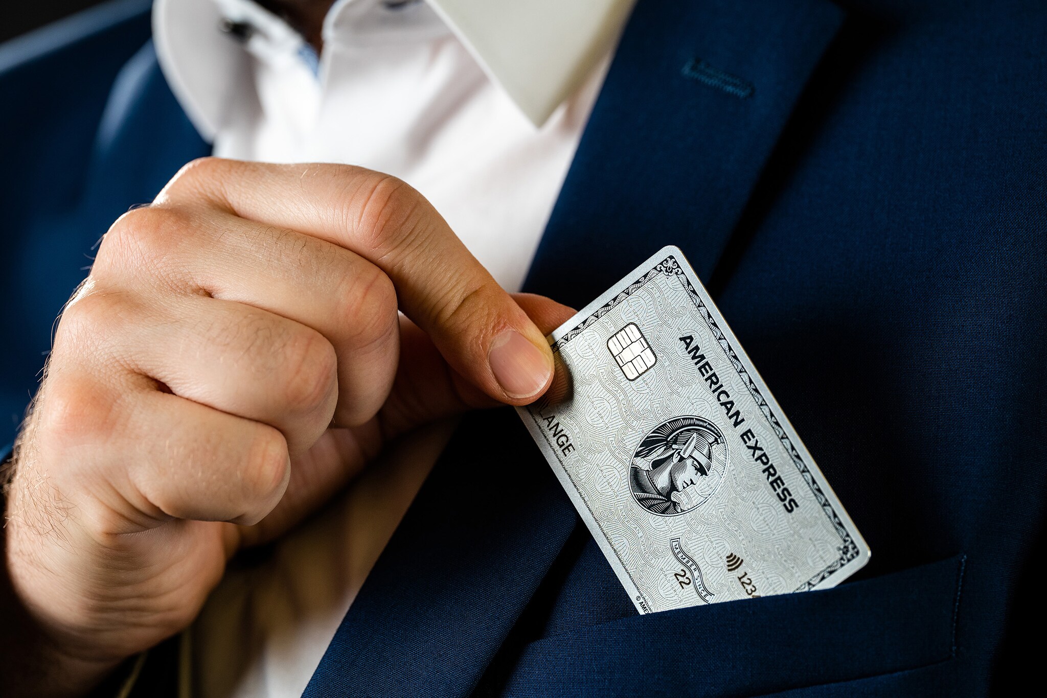 Eine Person steckt eine Kreditkarte in die Brusttasche eines Sakkos Eine Person steckt eine Kreditkarte in die Brusttasche eines Sakkos