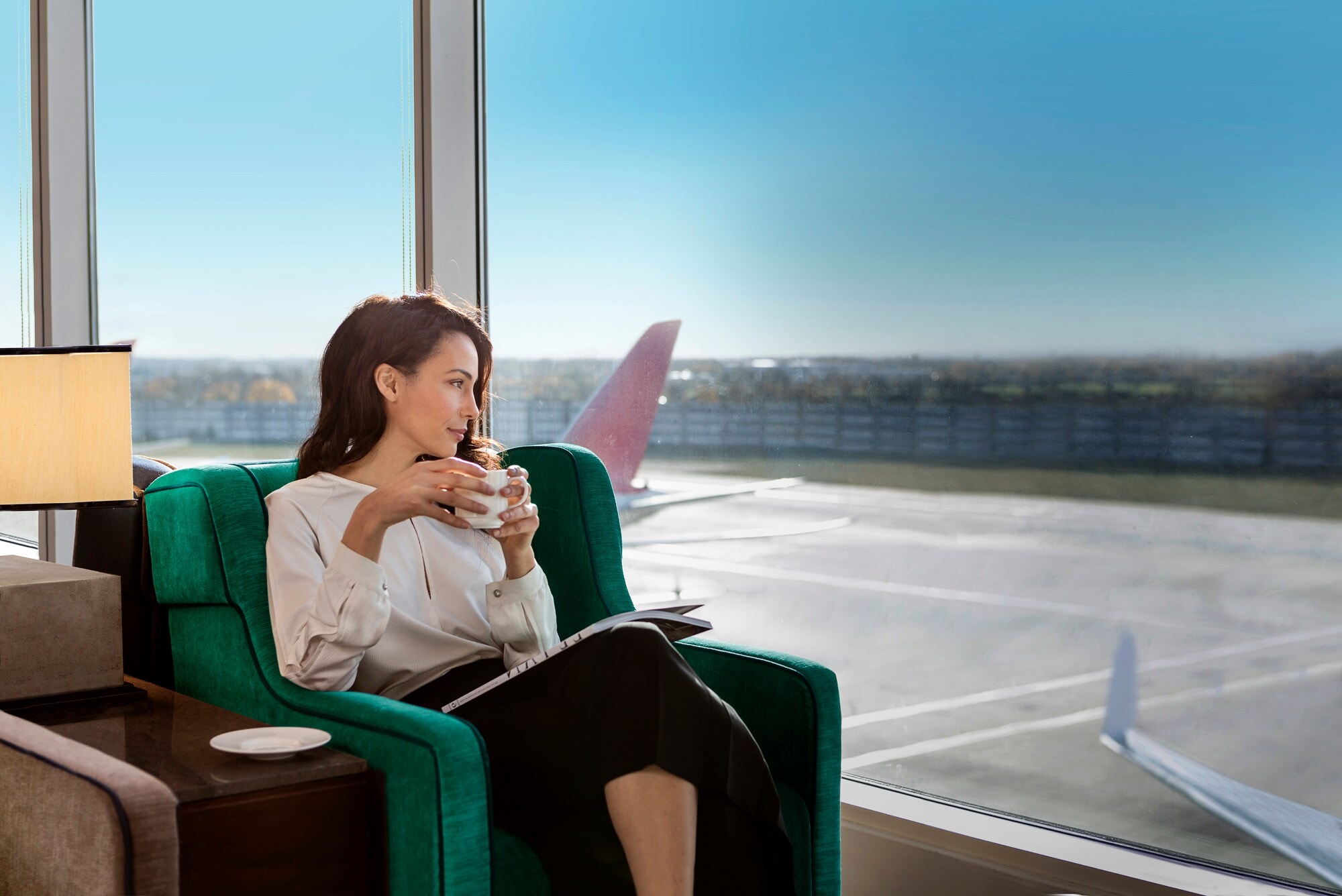 Eine Frau hält in einer Airport-Lounge eine Tasse Kaffee in der Hand und schaut aufs Rollfeld. Eine Frau hält in einer Airport-Lounge eine Tasse Kaffee in der Hand und schaut aufs Rollfeld.
