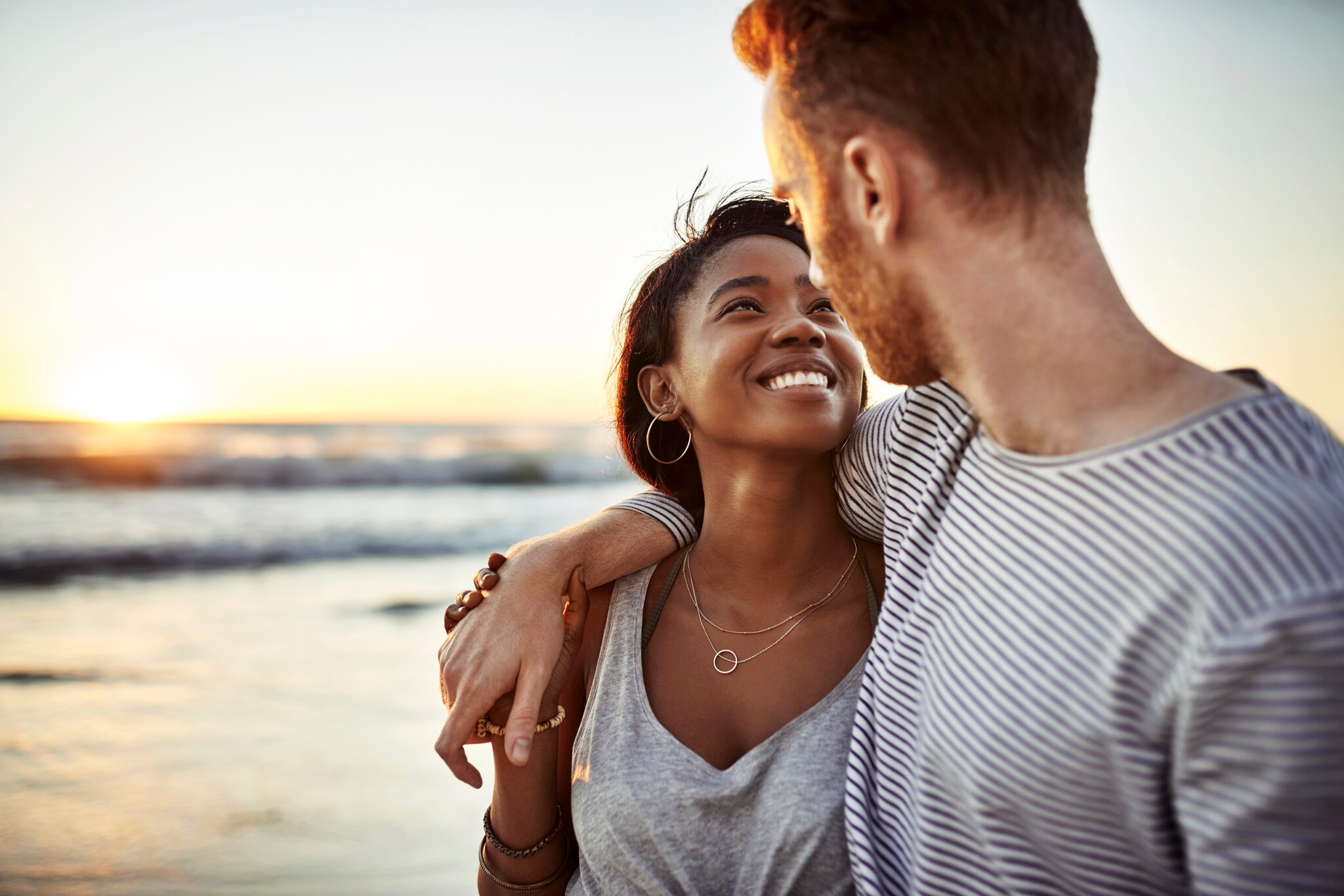 Nahaufnahme eines jungen Paares, das sich glücklich lächelnd am Meer anschaut
