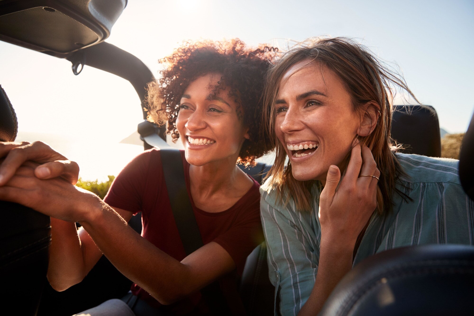 Nahaufnahme von zwei jungen, lachenden Frauen mit wehenden Haaren auf dem Rücksitz eines Cabriolets. Nahaufnahme von zwei jungen, lachenden Frauen mit wehenden Haaren auf dem Rücksitz eines Cabriolets.