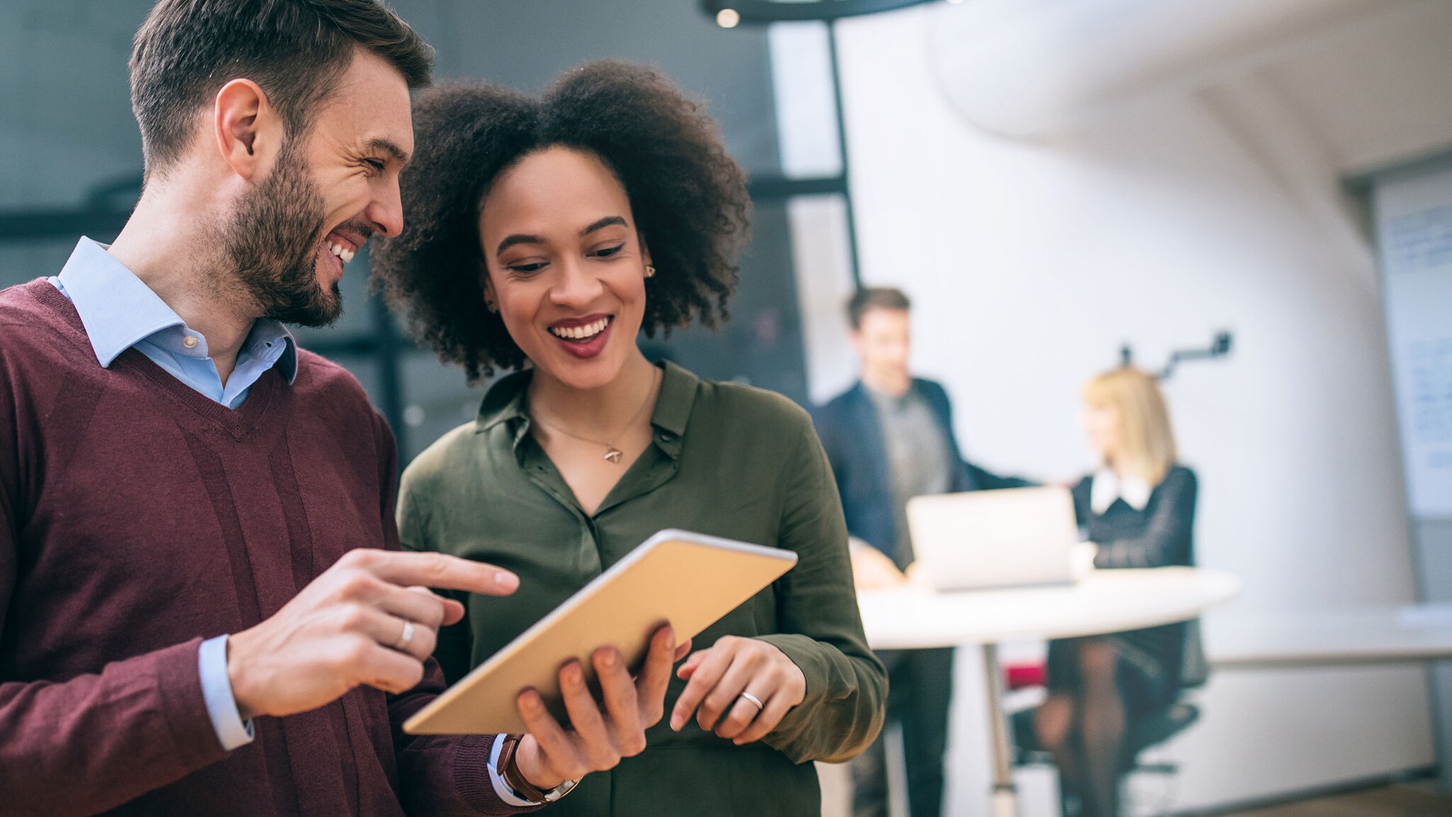 Zwei Kollegen stehen zusammen und schauen gemeinsam auf ein Tablet in einem Büro.
