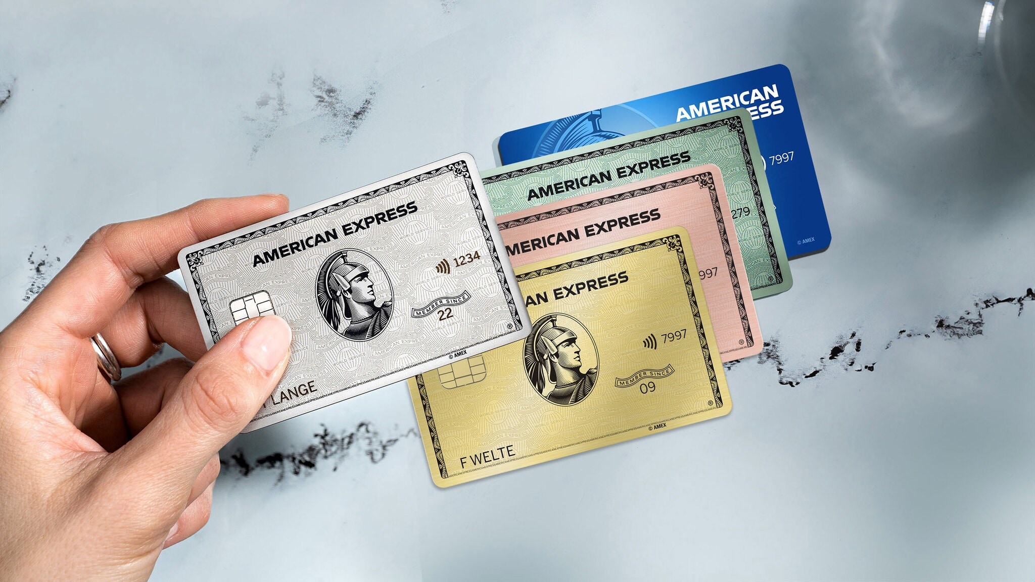 Eine Hand hält eine American Express Platinum Kreditkarte über drei weitere Kreditkarten in unterschiedlichen Farben auf einem Marmortisch. Eine Hand hält eine American Express Platinum Kreditkarte über drei weitere Kreditkarten in unterschiedlichen Farben auf einem Marmortisch.