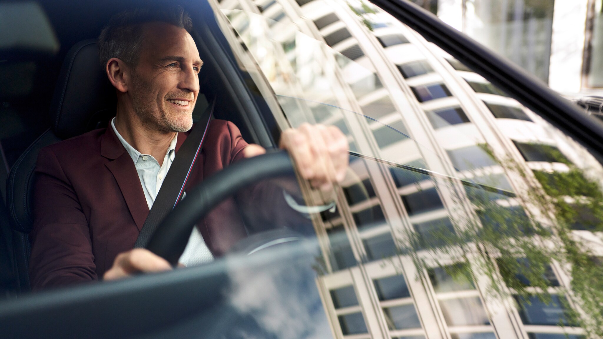 Leasing American Express Carbon Card Premium Ein Mann am Steuer eines BMW, in der Windschutzscheibe spiegelt sich ein Gebäude in urbaner Umgebung.