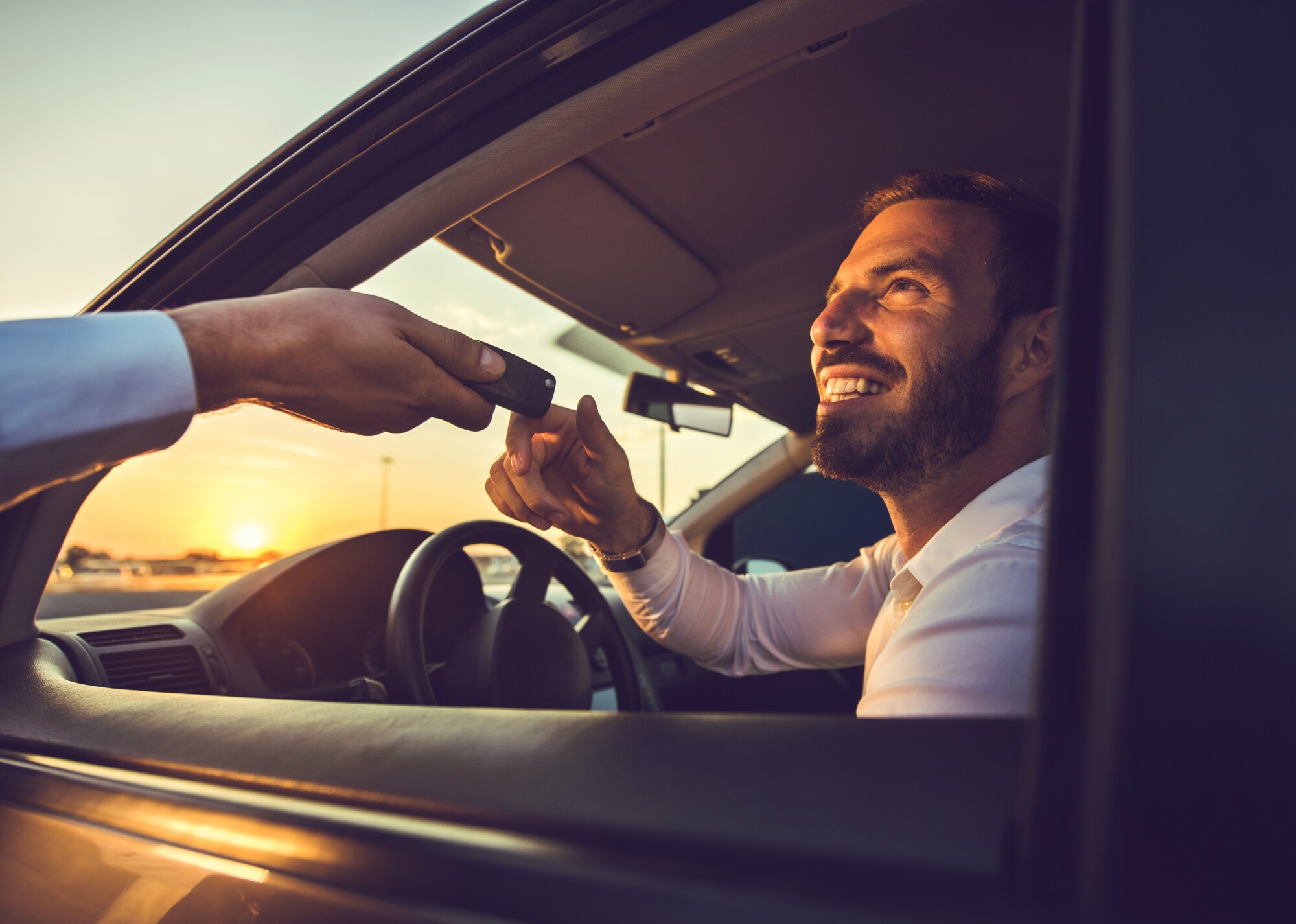 Ein Mann nimmt am Steuer eines Mietwagens den Autoschlüssel durch das geöffnete Fenster entgegen. Ein Mann nimmt am Steuer eines Mietwagens den Autoschlüssel durch das geöffnete Fenster entgegen.