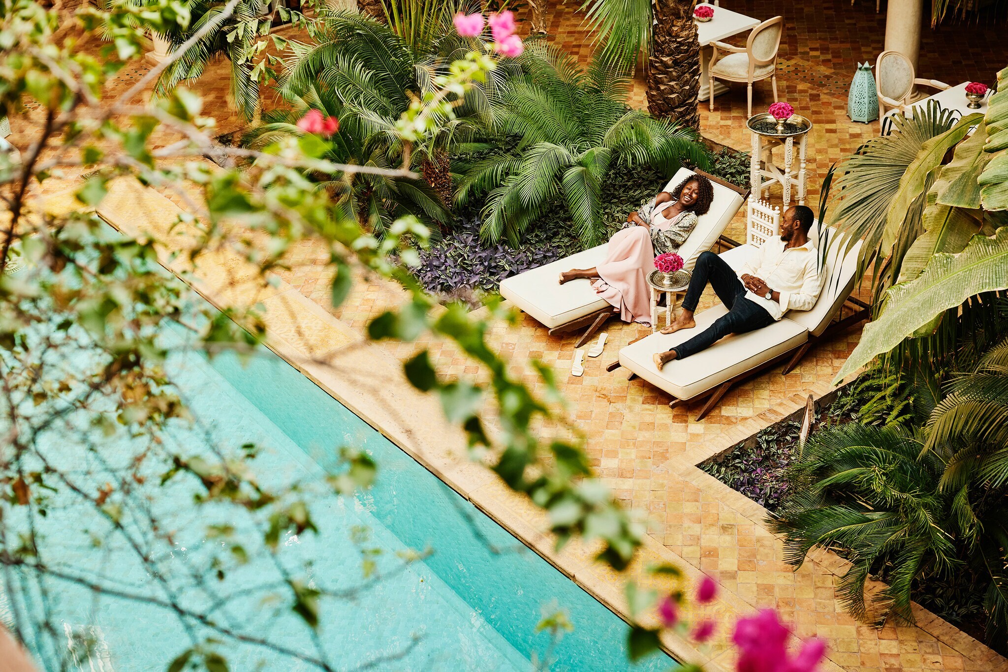 Aufsicht eines elegant gekleideten Paares auf Sonnenliegen an einem Pool auf der Terrasse eines Boutiquehotels.