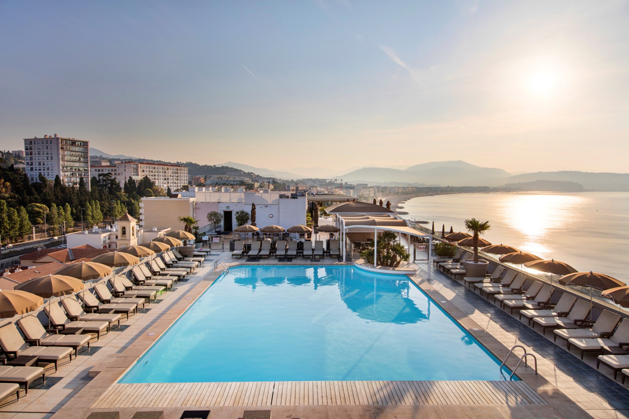 Ein von Sonnenliegen gesäumter Pool am Meer Ein von Sonnenliegen gesäumter Pool am Meer