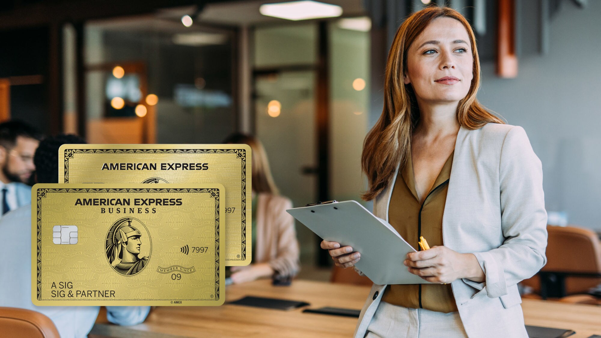 Eine Geschäftsfrau mit Klemmbrett in den Händen lehnt an einem Konferenztisch mit Personen in einem modernen Büro und schaut zufrieden in die Ferne, daneben eine Collage zweier Freisteller von goldenen Kreditkarten von American Express. Eine Geschäftsfrau mit Klemmbrett in den Händen lehnt an einem Konferenztisch mit Personen in einem modernen Büro und schaut zufrieden in die Ferne, daneben eine Collage zweier Freisteller von goldenen Kreditkarten von American Express.