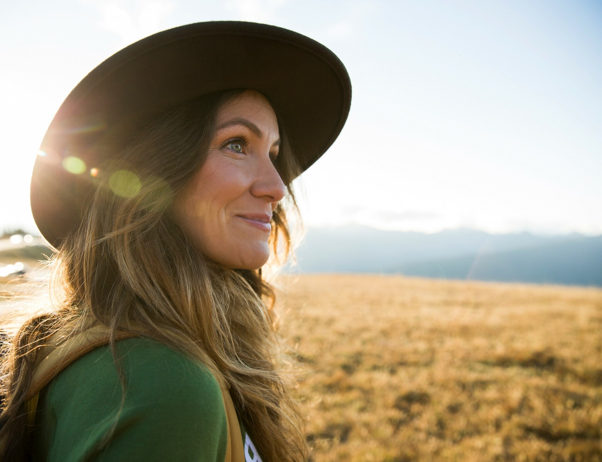 Eine junge Frau mit Hut schaut auf einer Wanderung in die Ferne