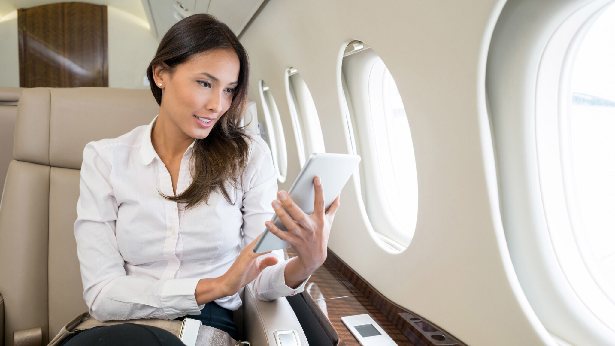 Geschäftsfrau sitzt auf einem Business-Platz im Flugzeug und blickt auf ein Tablet.