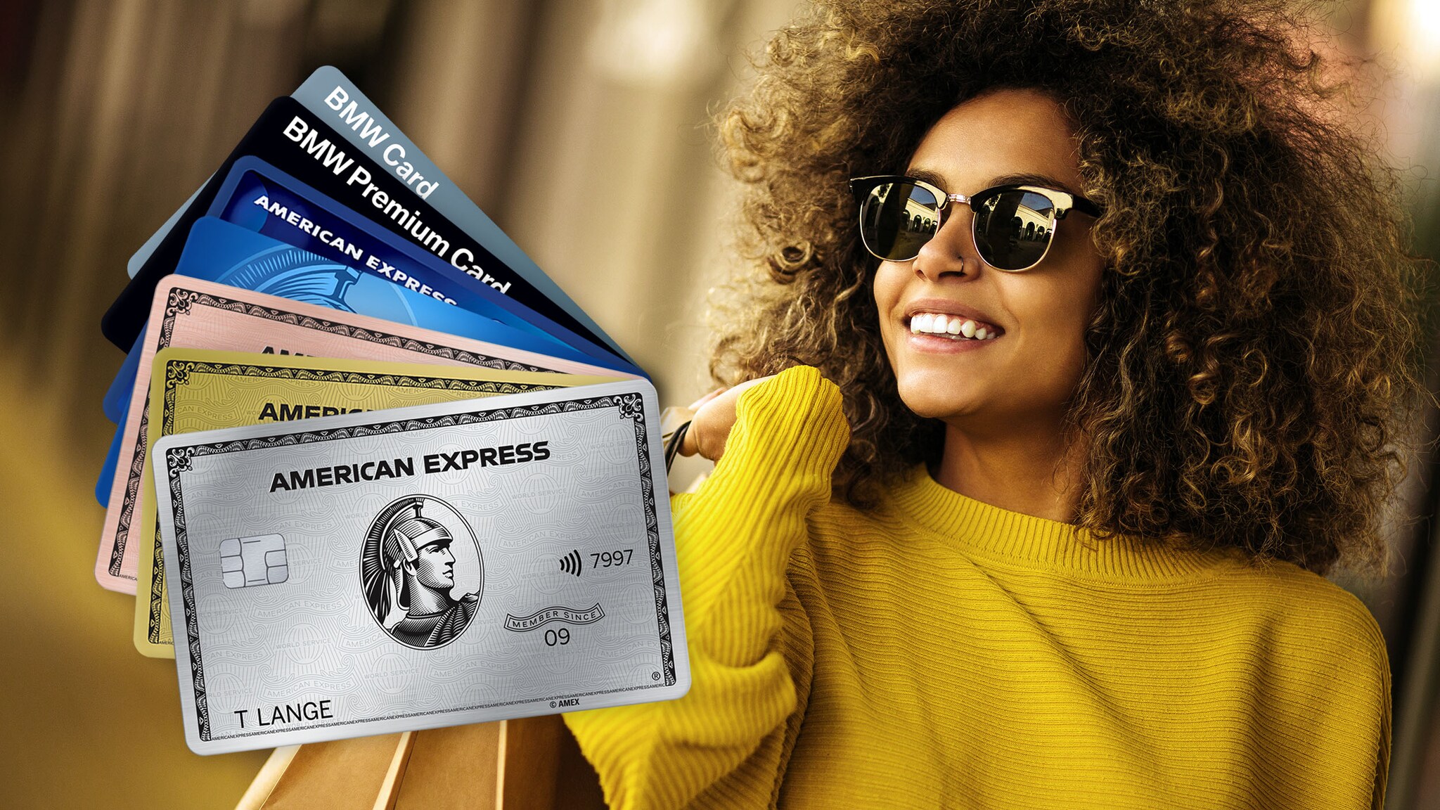 Sieben aufgefächerte Kreditkarten von American Express, im Hintergrund eine lachende Frau mit Sonnenbrille und Einkaufstüten über der Schulter. Sieben aufgefächerte Kreditkarten von American Express, im Hintergrund eine lachende Frau mit Sonnenbrille und Einkaufstüten über der Schulter.