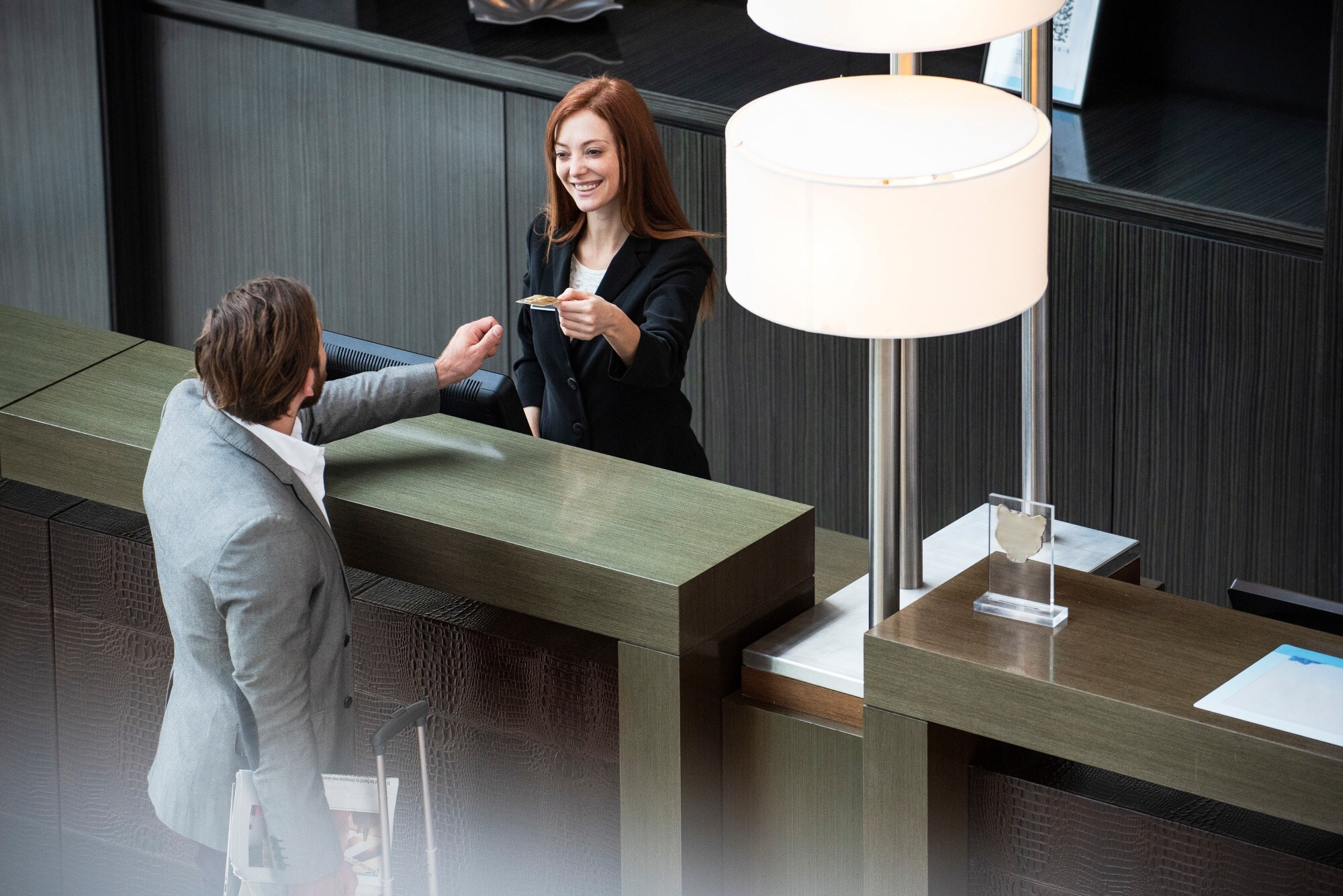 Ein Geschäftsmann hinterlegt eine Kreditkarte bei einer Rezeptionistin beim Einchecken im Hotel Ein Geschäftsmann hinterlegt eine Kreditkarte bei einer Rezeptionistin beim Einchecken im Hotel