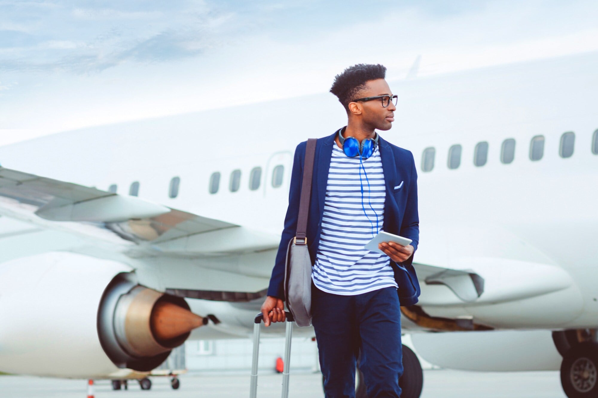 Ein junger, stylisher Geschäftsmann mit Reisegepäck vor einem Flugzeug Ein junger, stylisher Geschäftsmann mit Reisegepäck vor einem Flugzeug