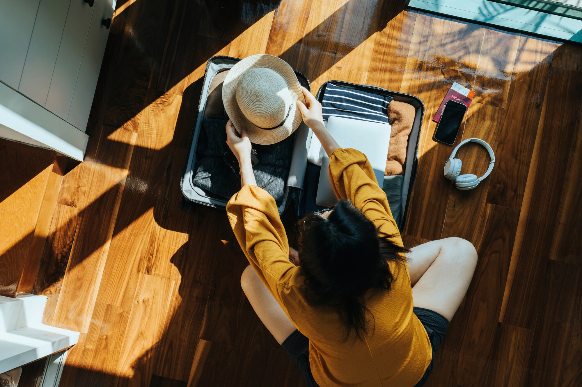 Aufsicht einer jungen Frau, die auf einem Holzfußboden in einem Zimmer einen kleinen Reisekoffer packt. Aufsicht einer jungen Frau, die auf einem Holzfußboden in einem Zimmer einen kleinen Reisekoffer packt.