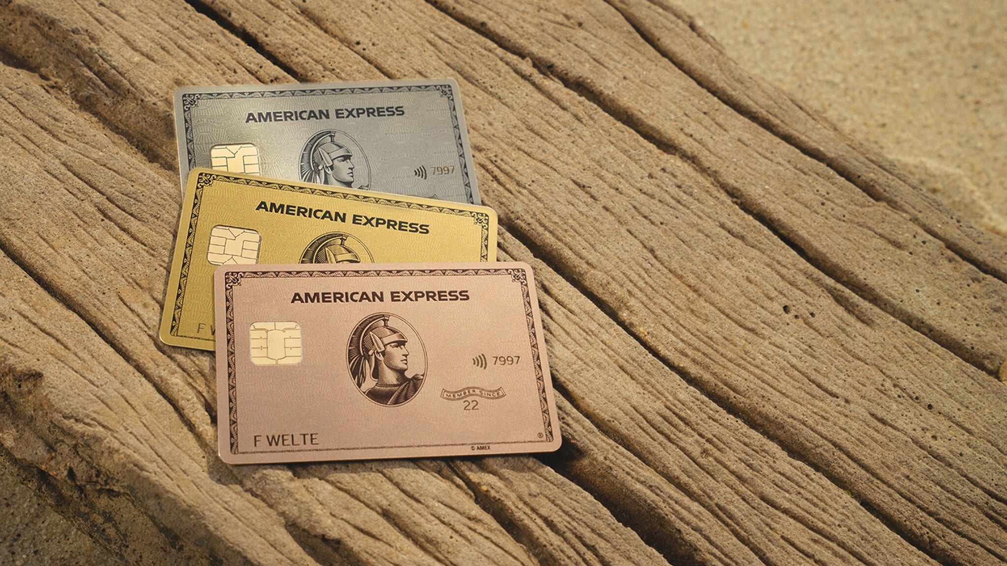Die American Express Gold Card Rosé, die Gold Card und die Platinum Card liegen auf einer Holzfläche. Die American Express Gold Card Rosé, die Gold Card und die Platinum Card liegen auf einer Holzfläche.