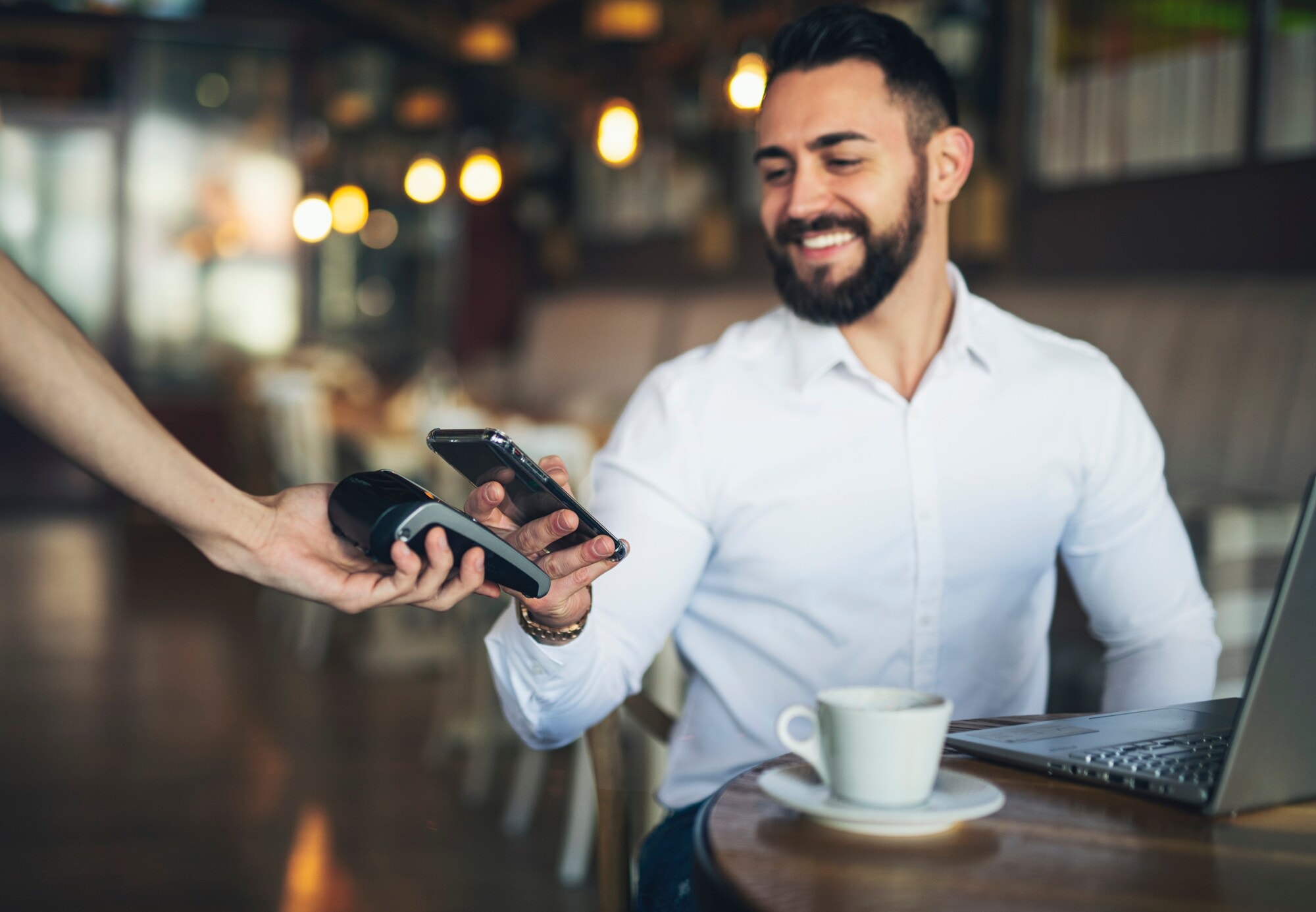Ein junger Mann bezahlt kontaktlos mit seinem Smartphone in einem Café Ein junger Mann bezahlt kontaktlos mit seinem Smartphone in einem Café