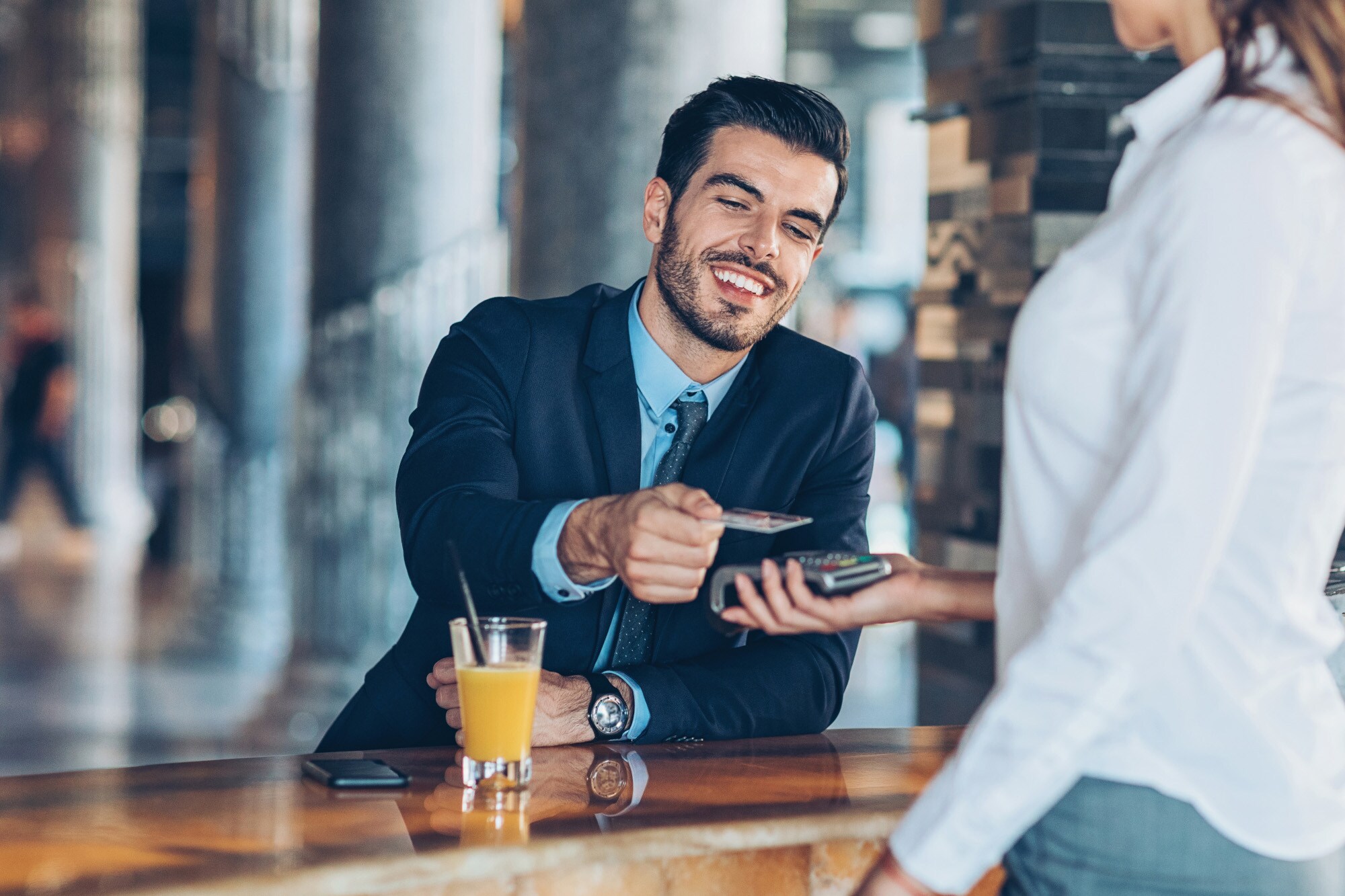 Ein junger Geschäftsmann bezahlt kontaktlos mit seiner Kreditkarte an einer Hotelbar.