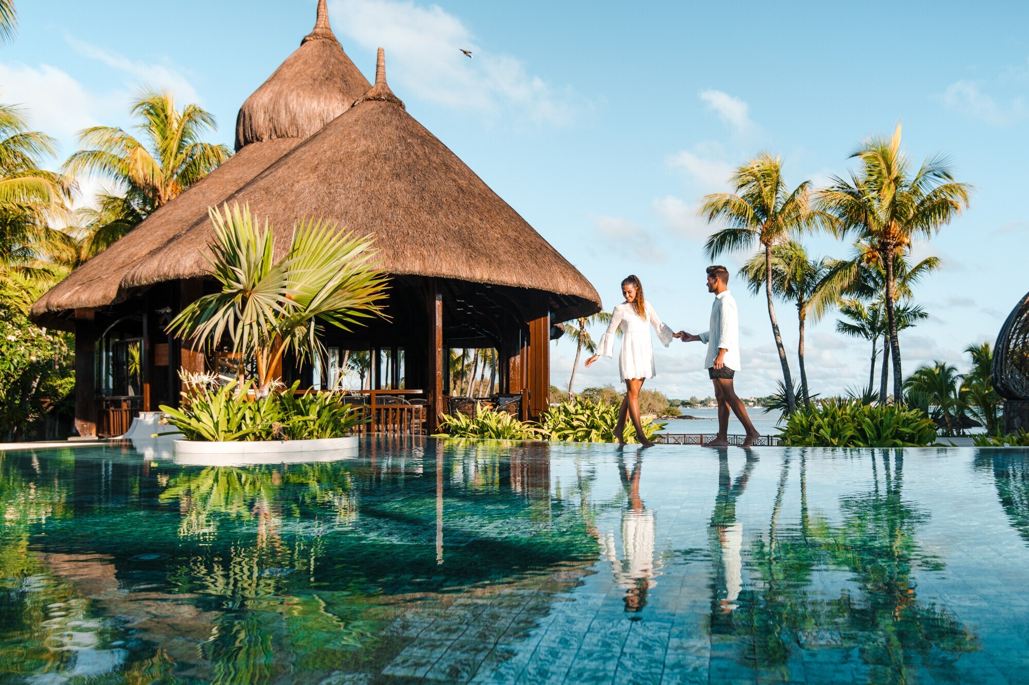 Ein Paar steht an einem luxuriösen Hotelpool am Meer in tropischer Umgebung.