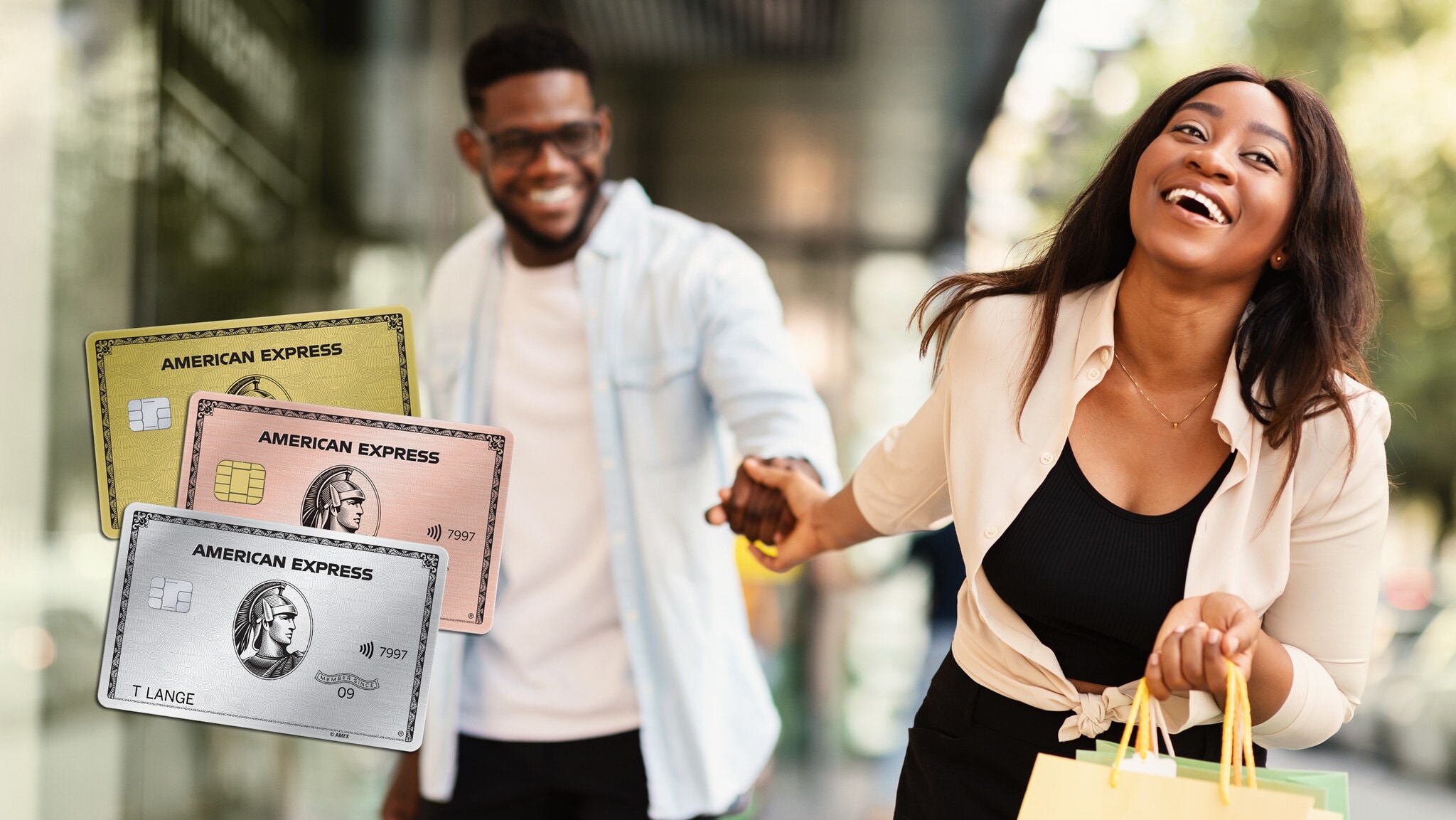 Ein Mann und eine Frau laufen Hand in Hand lachend vor einem Geschäft, im Vordergrund sieht man drei Kreditkarten von American Express.