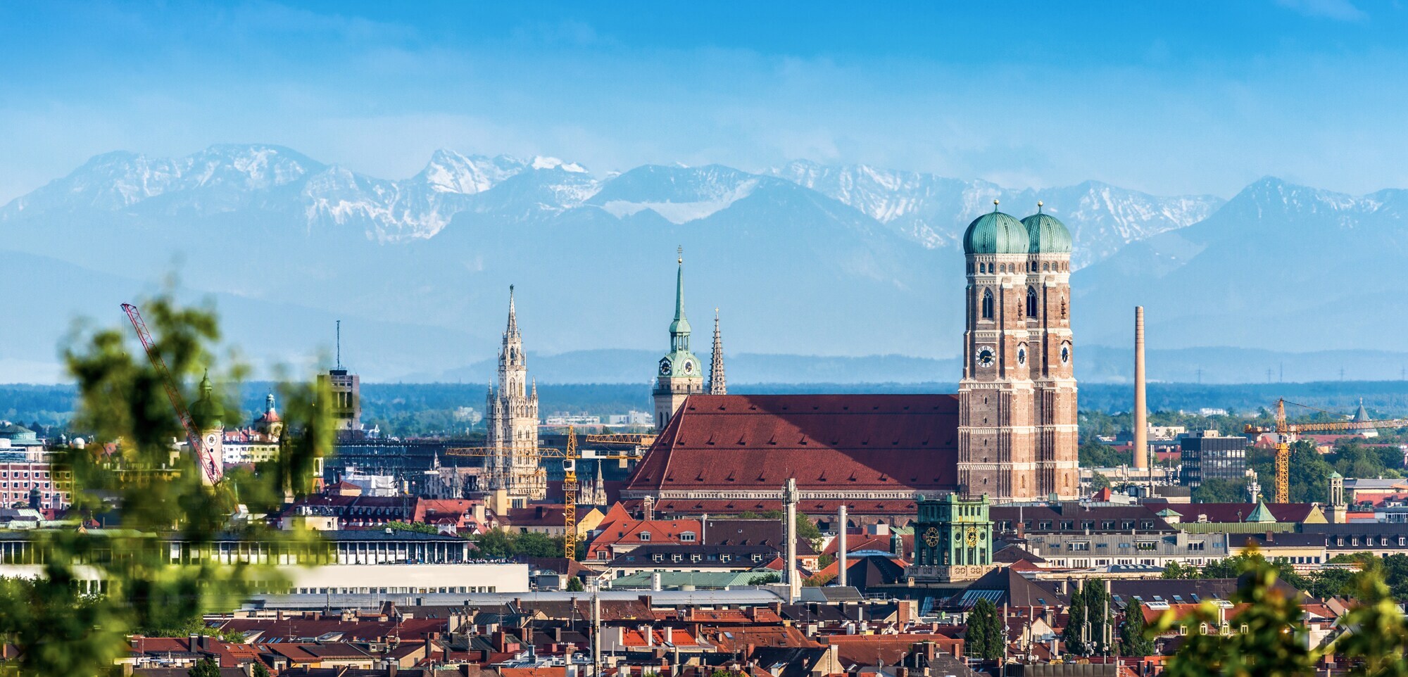 Ein Blick über München mit den Alpen im Hintergrund ist zu sehen.