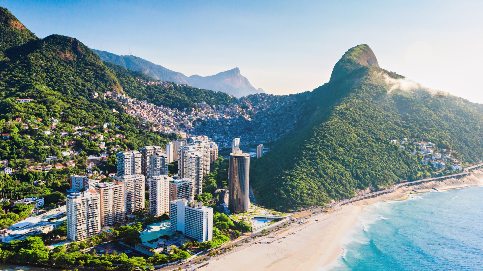 An einem Strand liegt eine Stadt mit Hochhäusern und riesigen Bergen.