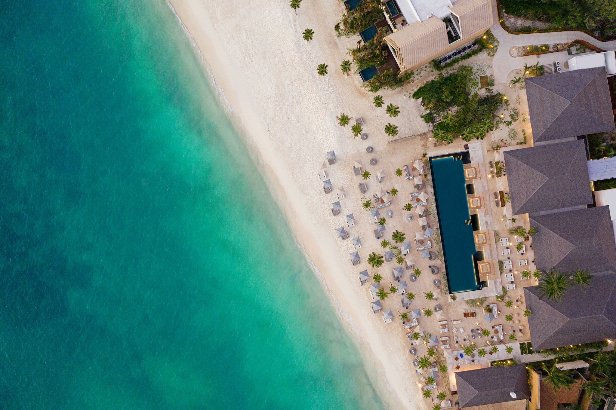 Hotelresort mit Pool und Sanstrand am türkisblauen Meer aus der Vogelperspektive.