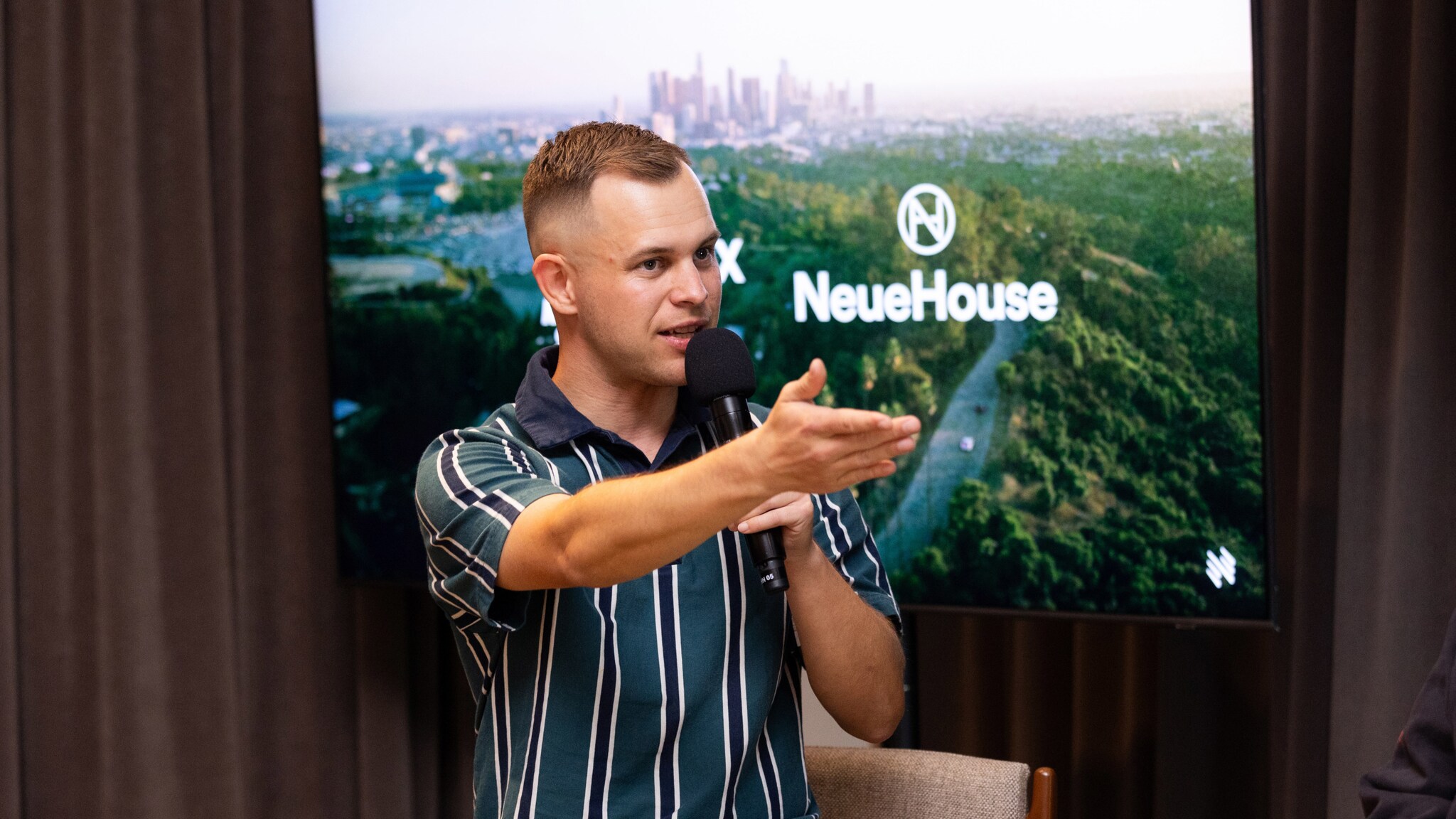 Porträt von Benjamin Diedering mit erhobener Hand und Mikrofon während einer Präsentation.