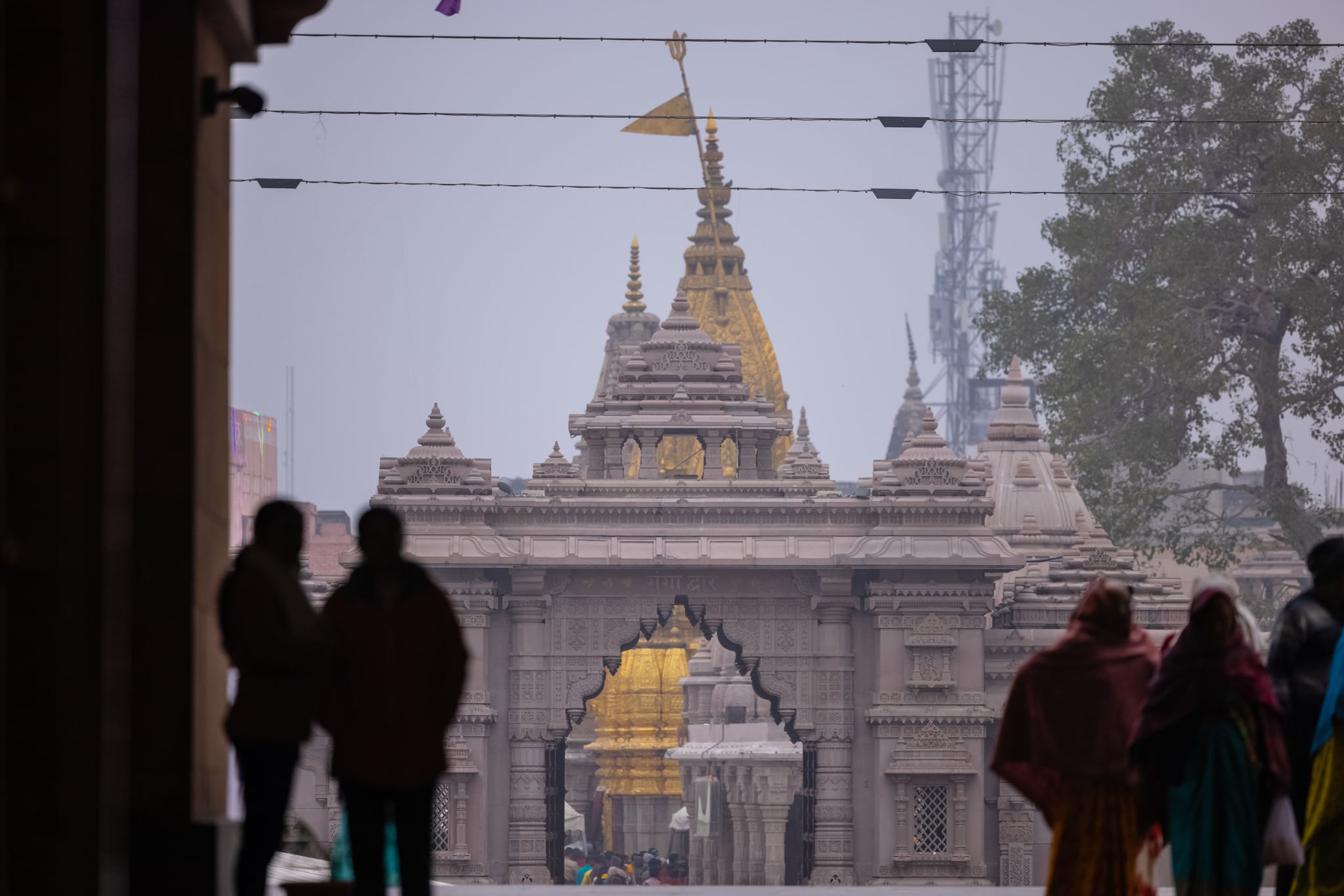 Blick auf den Kashi Vishwanath Tempel mit seinem vergoldeten Turm mit den dunklen Umrissen von Menschen im Vordergrund. Blick auf den Kashi Vishwanath Tempel mit seinem vergoldeten Turm mit den dunklen Umrissen von Menschen im Vordergrund.