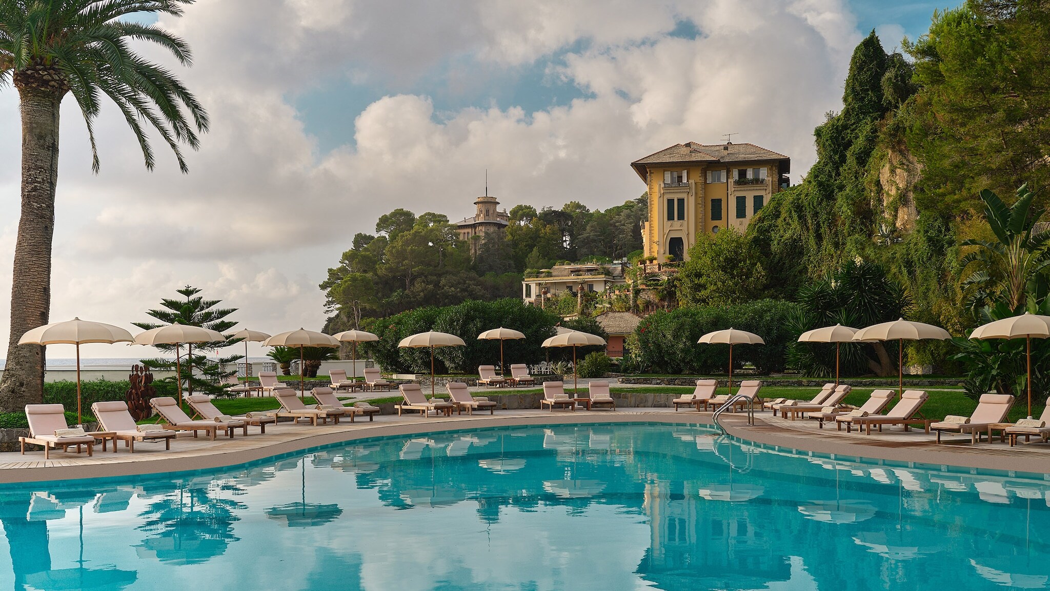 Luxuriöse Hotelterrasse mit Pool und Liegestühlen an einer mediterranen Küste.