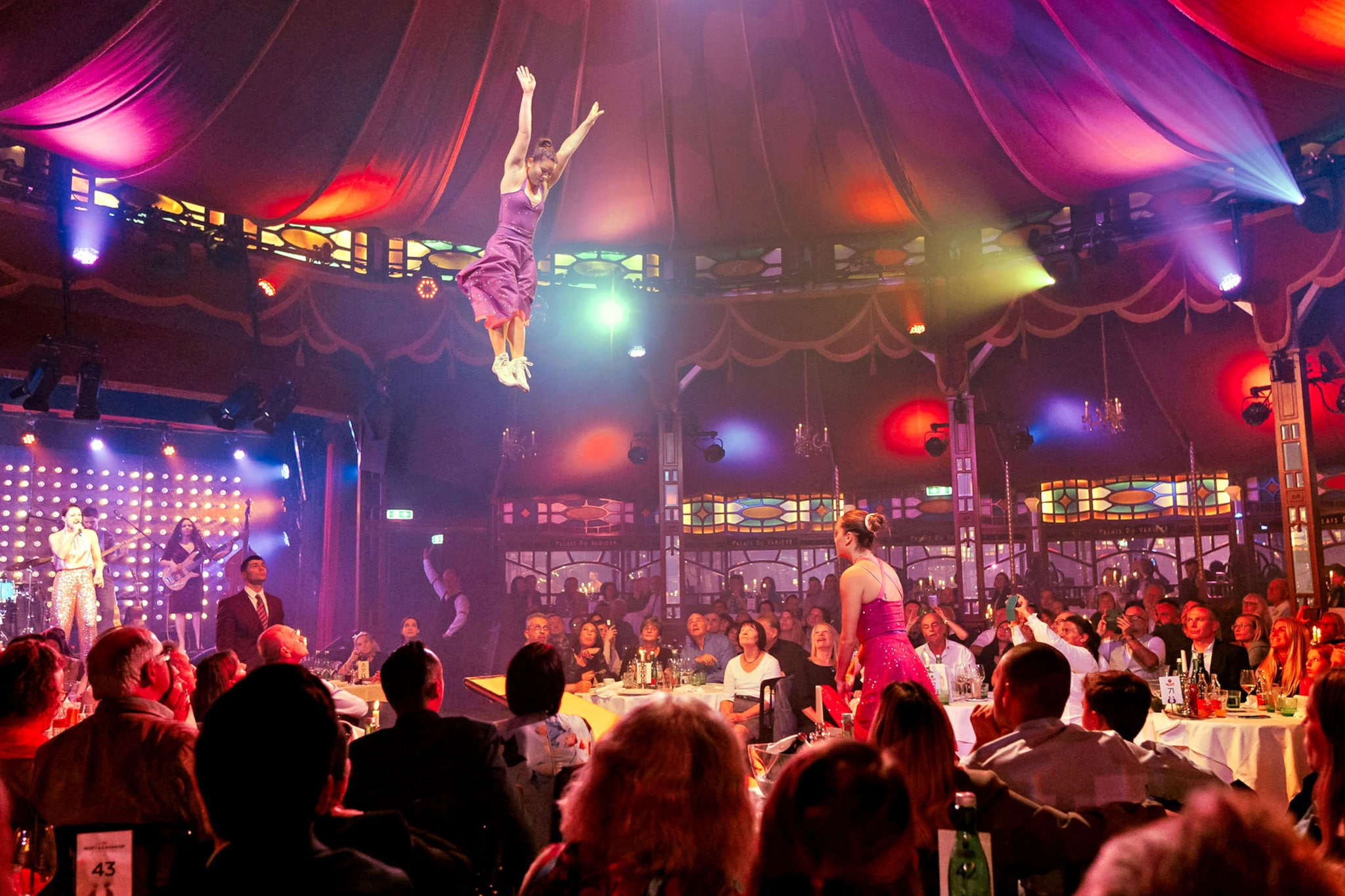 Personen sitzen beim Dinner an Tischen in einem Spiegelzelt während einer Show mit Akrobatinnen.