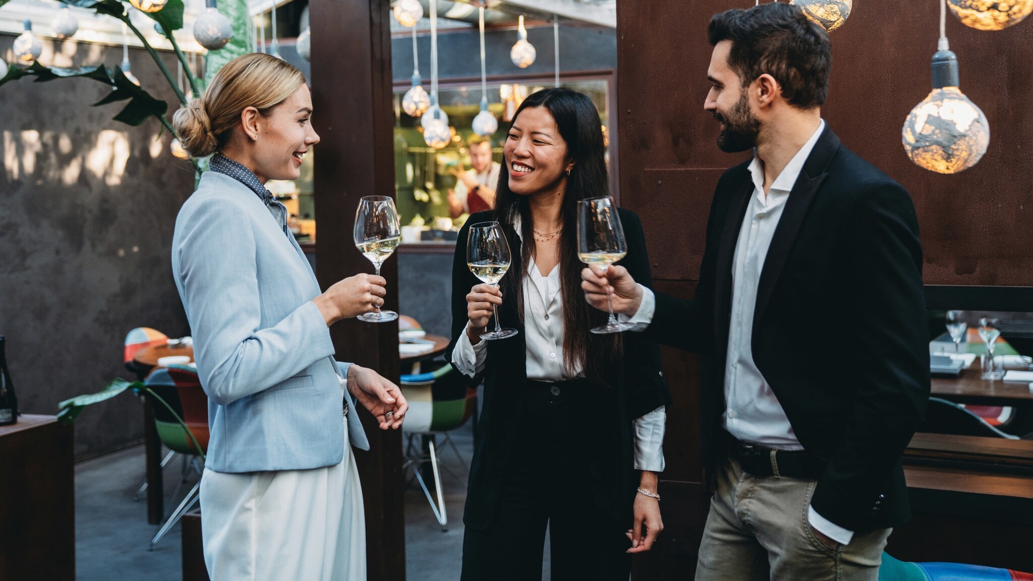 Drei Personen in eleganter Kleidung und mit Weingläsern in den Händen stehen beieinander und unterhalten sich. Drei Personen in eleganter Kleidung und mit Weingläsern in den Händen stehen beieinander und unterhalten sich.