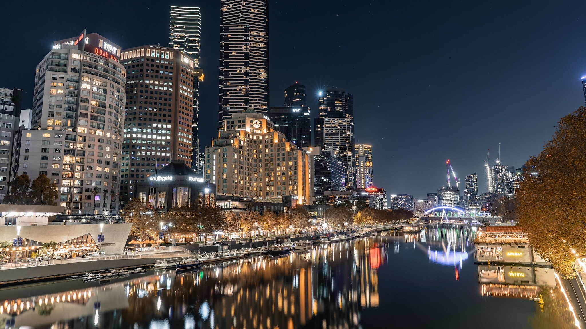 Beleuchtete Skyline mit Hochhäusern an einem Flussufer bei Nacht.