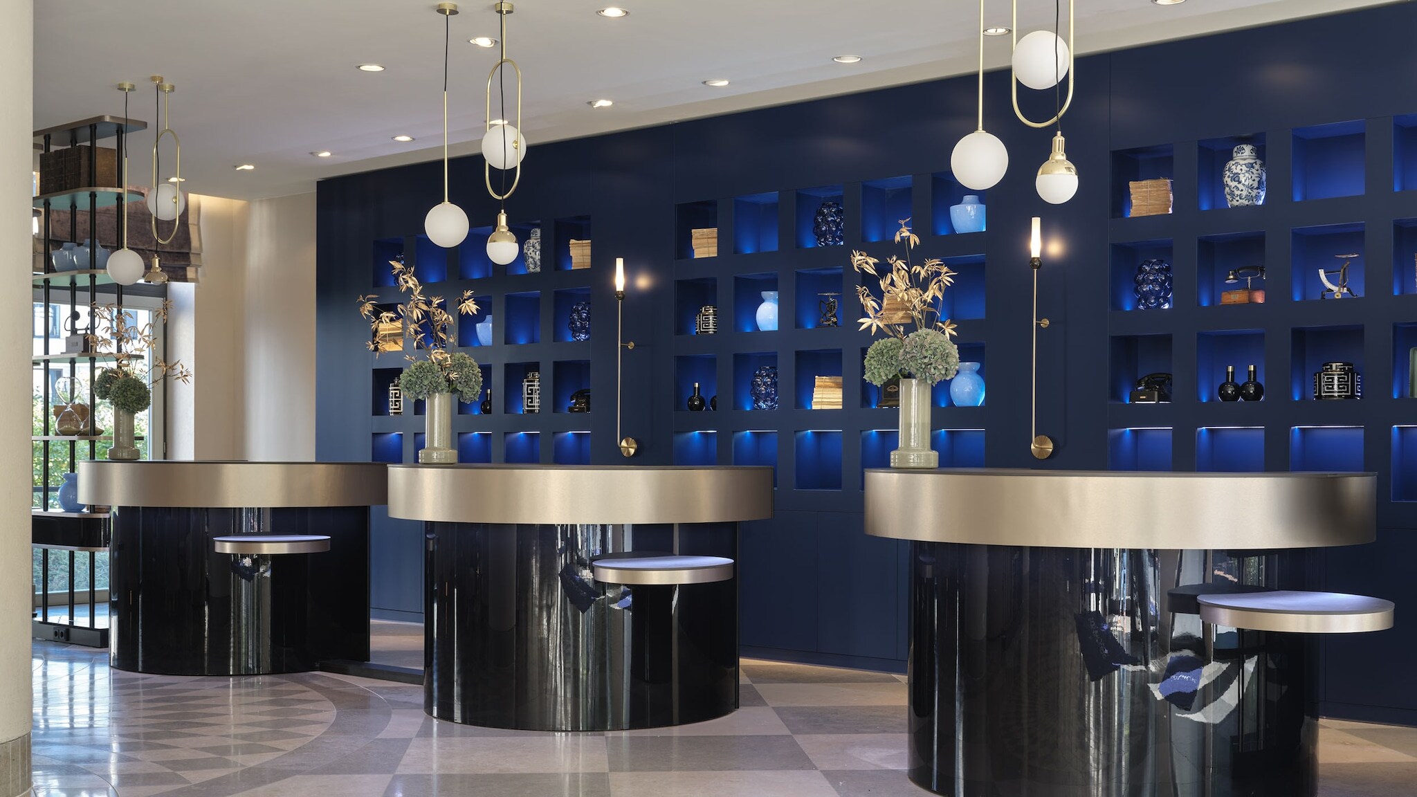 amex-magazin-hotel-posthouse-berlin Moderne Hotellobby mit runden Empfangstresen und Designelementen vor blauer Wand.