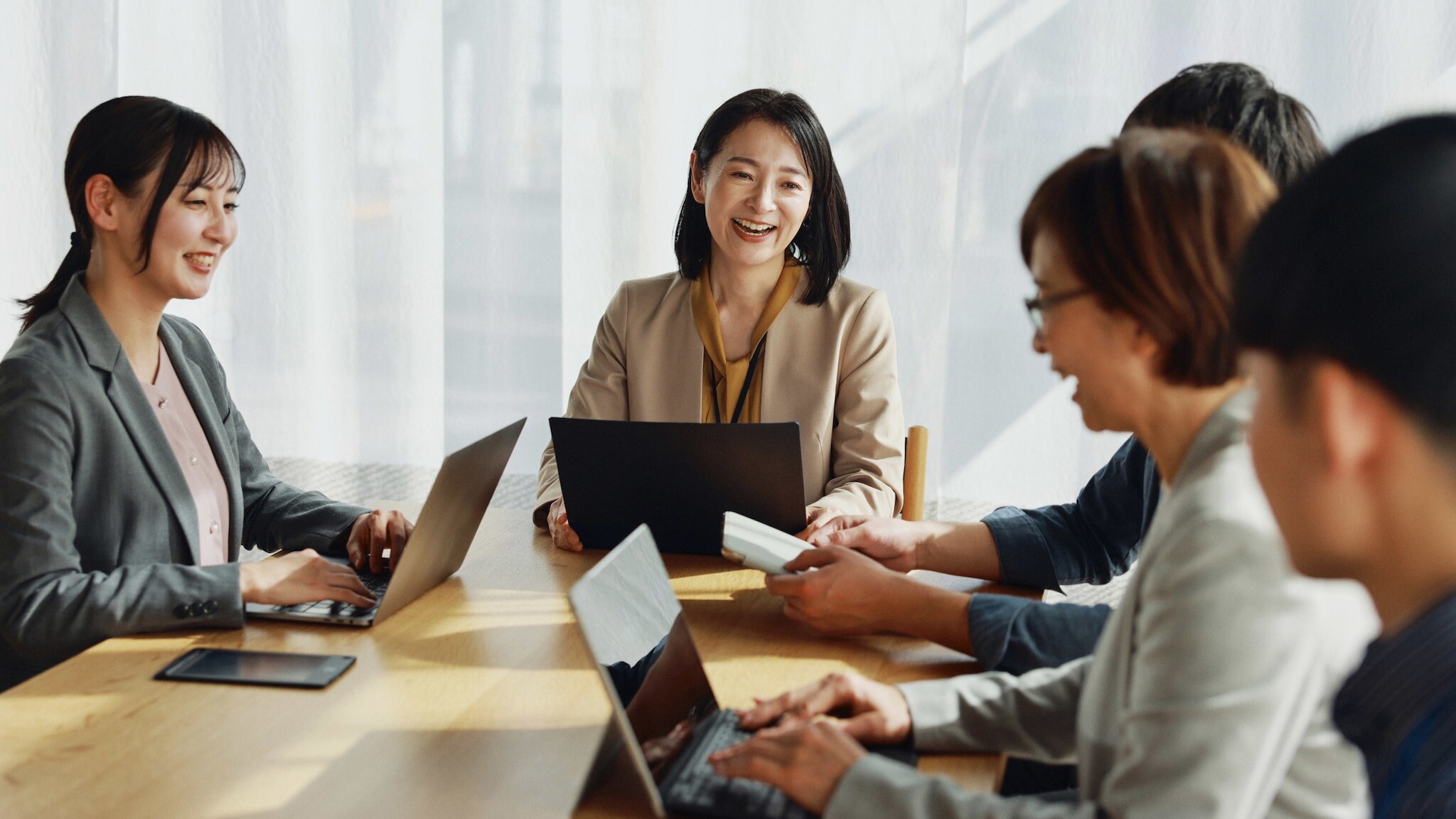 Eine Gruppe asiatischer Menschen sitzt lächelnd mit Laptops an einem Tisch.