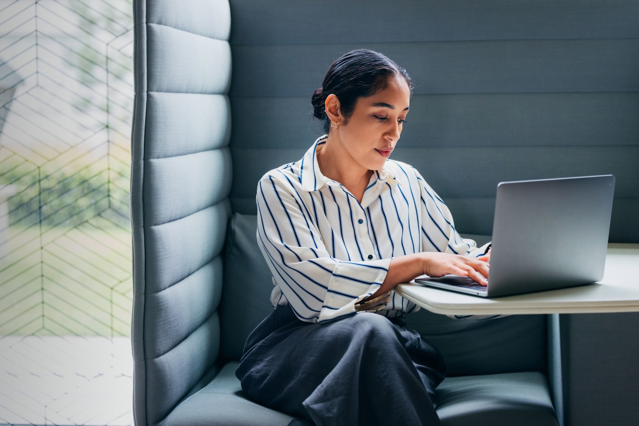 Eine Frau mit Laptop vor sich auf dem Tisch in einer gepolsterten Sitzecke.