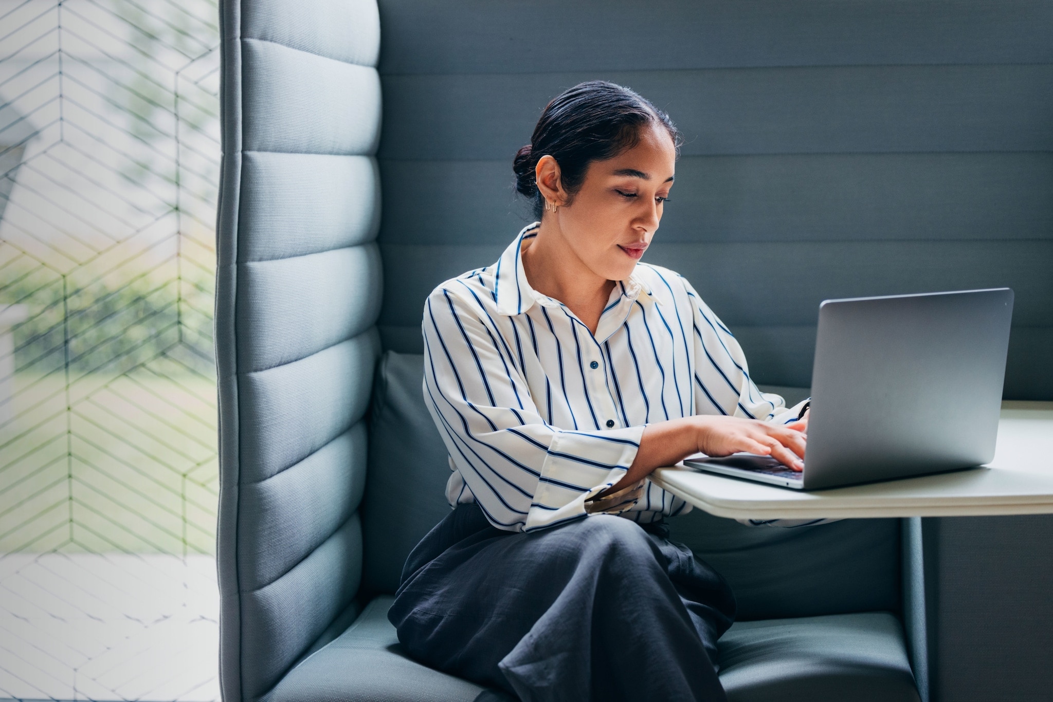 Eine Frau mit Laptop vor sich auf dem Tisch in einer gepolsterten Sitzecke. Eine Frau mit Laptop vor sich auf dem Tisch in einer gepolsterten Sitzecke.