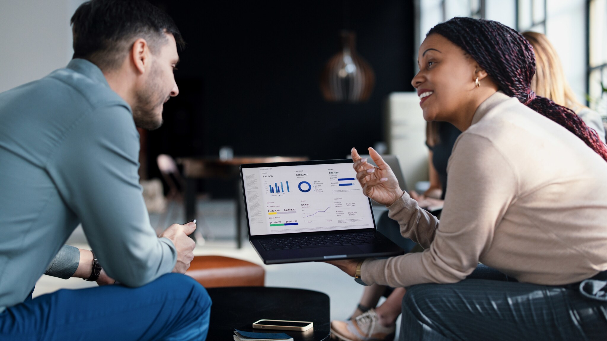 Profilansicht von zwei sitzenden Personen, die gemeinsam auf einen Laptop mit Diagrammen auf dem Display schauen.
