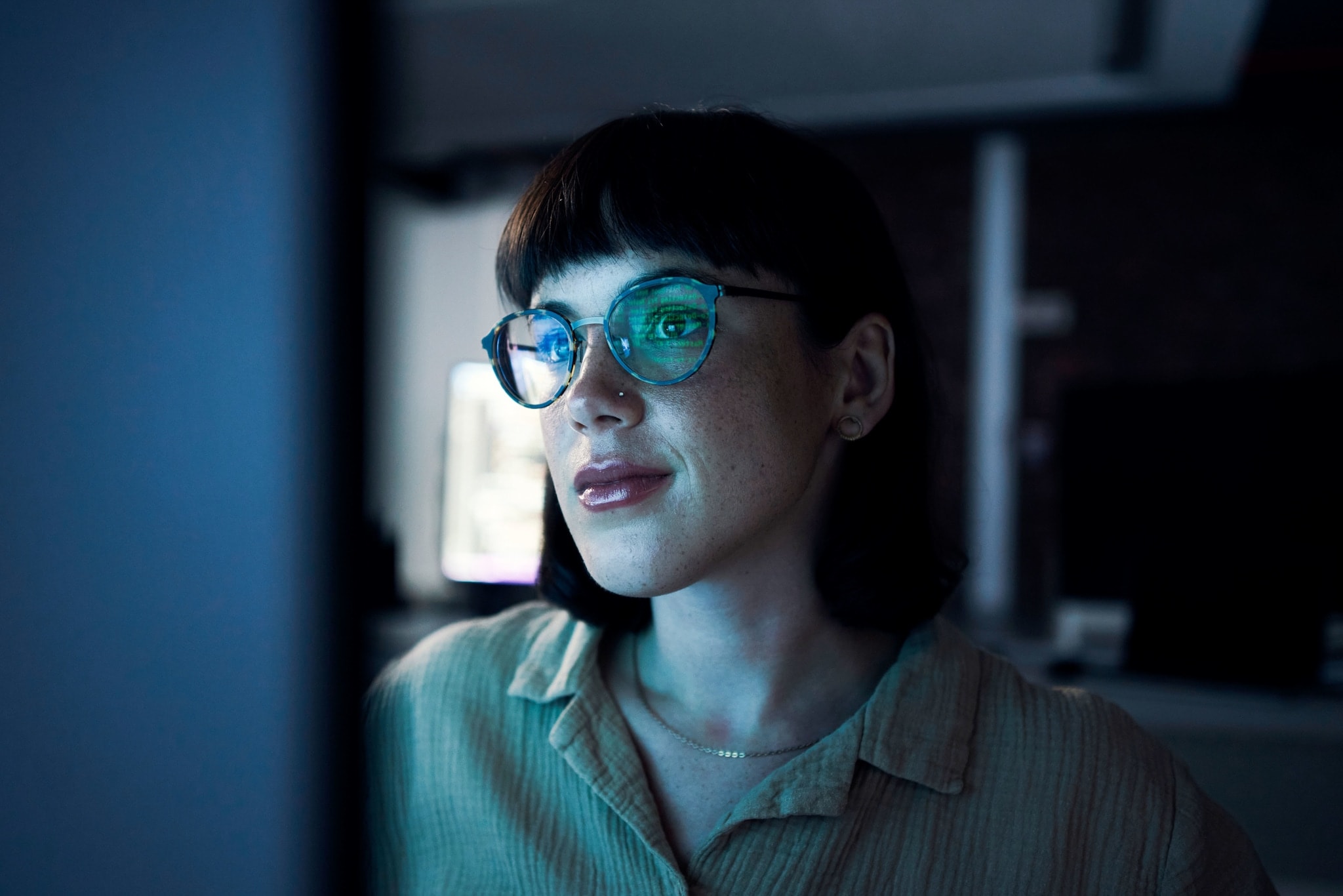 Eine Frau mit einer Brille in einem dunklen Raum vor einem Bildschirm. Eine Frau mit einer Brille in einem dunklen Raum vor einem Bildschirm.