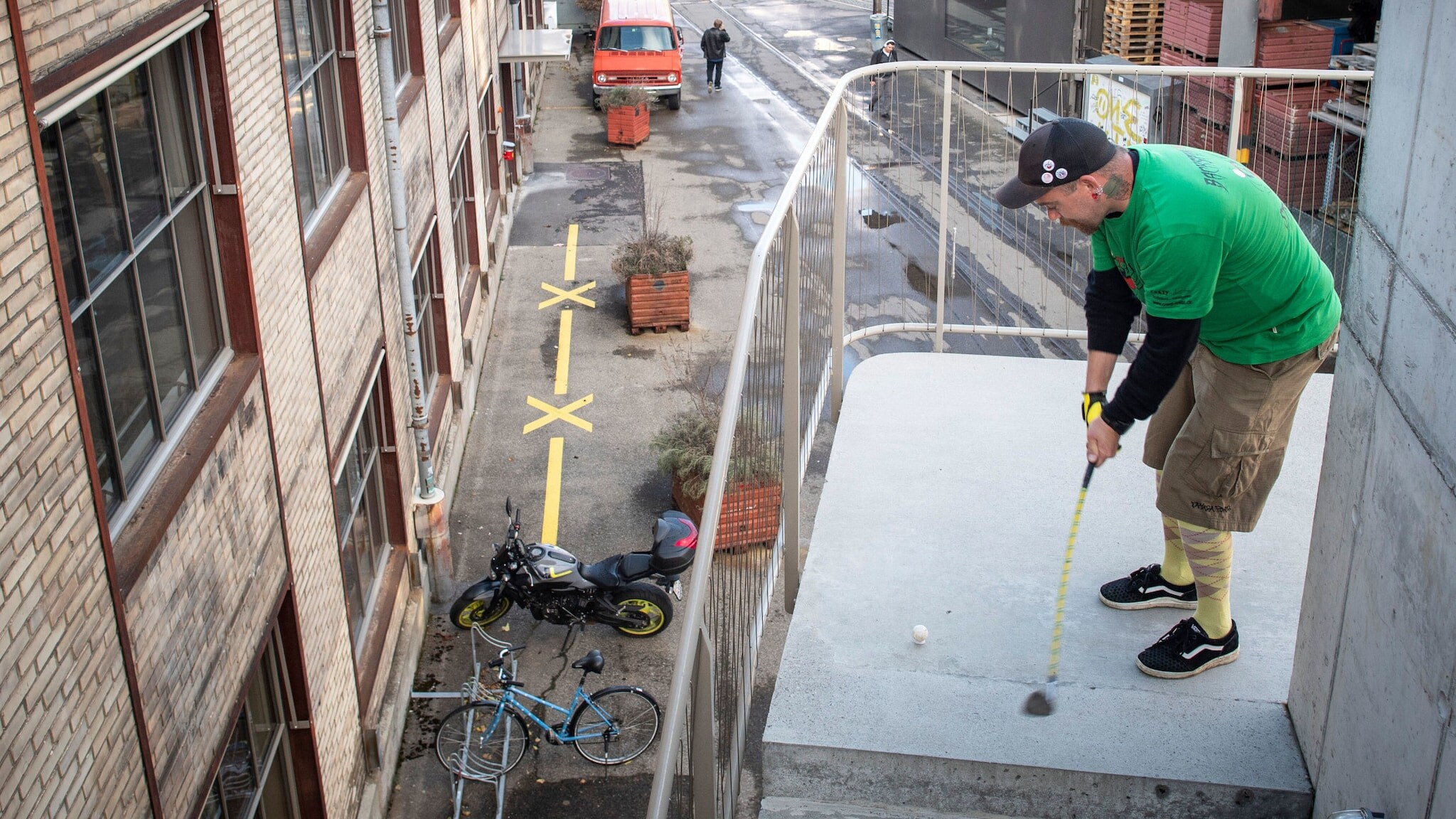 Ein Mann spielt Golf auf einer Außentreppe an einem Gebäude in einem Industriegebiet.