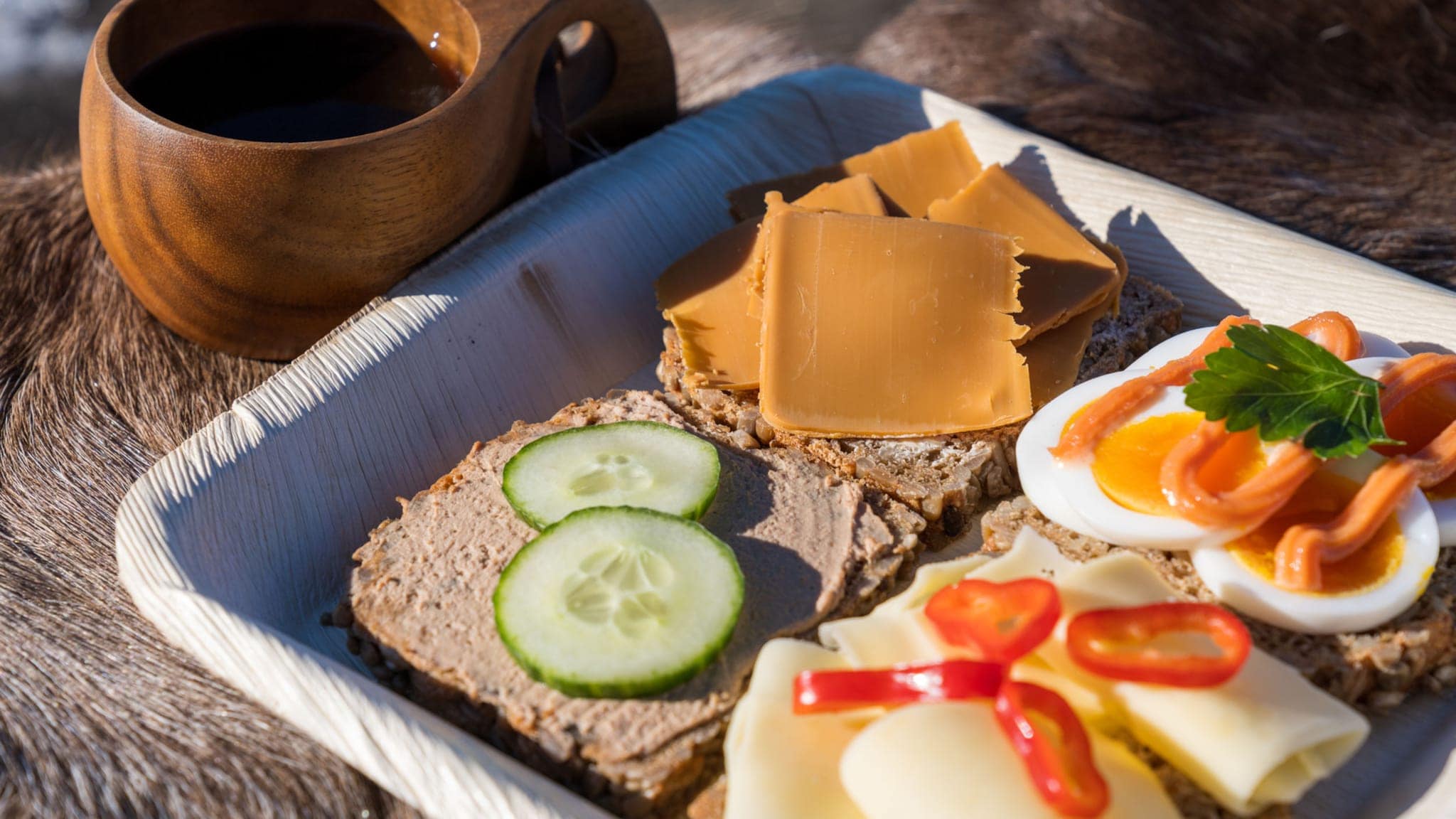Nahaufnahme einer Holzplatte mit unterschiedlich belegten Broten neben einem Kaffeebecher aus Holz. Nahaufnahme einer Holzplatte mit unterschiedlich belegten Broten neben einem Kaffeebecher aus Holz.