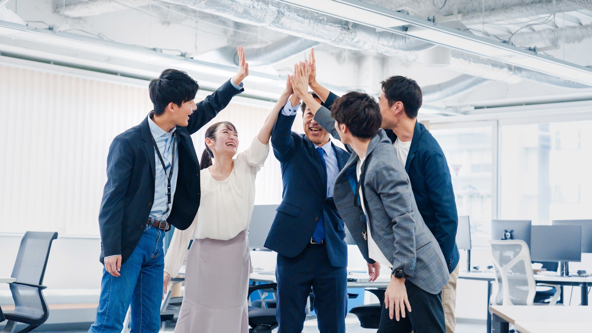 Fünf lächelnde asiatische Personen in Business-Kleidung in einem Büro schlagen ihre Hände in ihrer Mitte zusammen. Fünf lächelnde asiatische Personen in Business-Kleidung in einem Büro schlagen ihre Hände in ihrer Mitte zusammen.