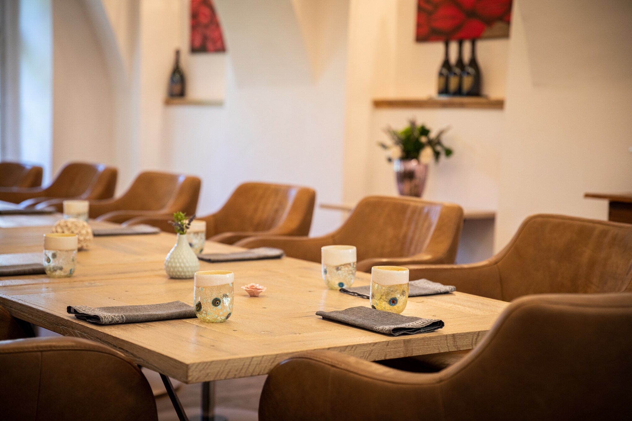 Gedeckte Holztische an denen cognacfarbenen Ledersessel stehen eines Sternerestaurants, im Hintergrund stehen Champagnerflaschen auf Regalen.