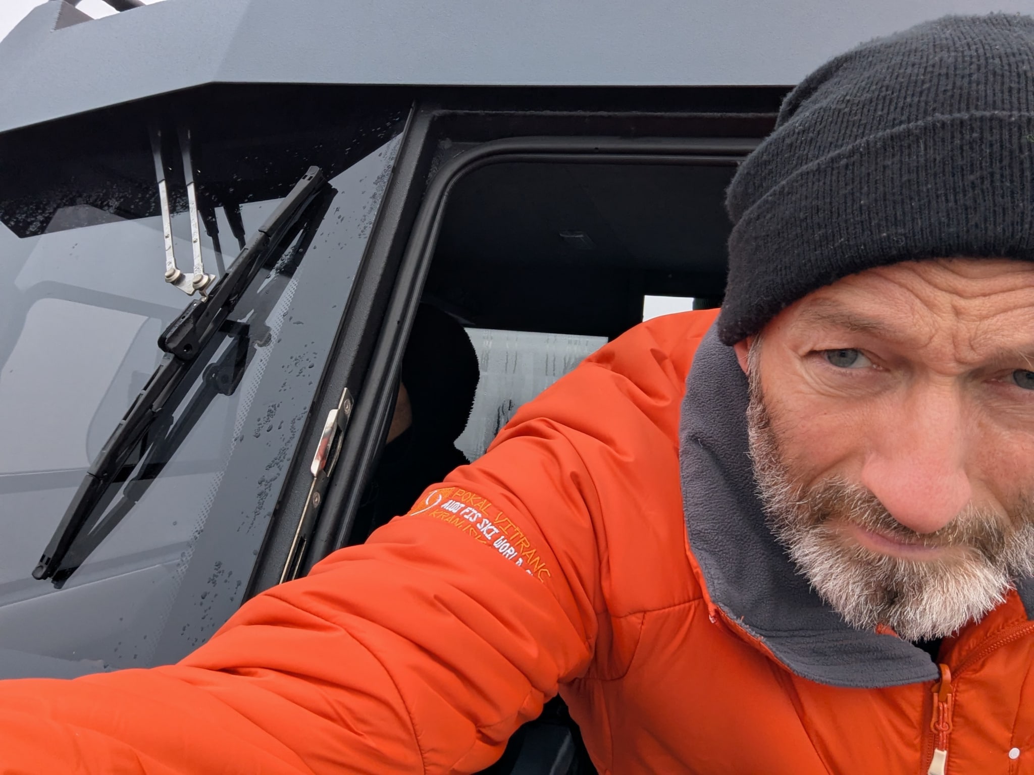 Person mit wetterfester Kleidung im Steuerhaus eines Motorboots mit regennassen Scheiben.