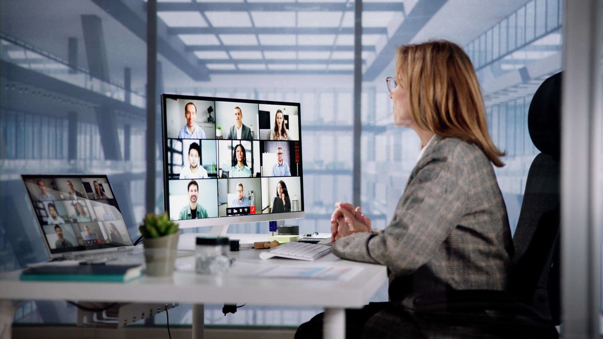 Profilansicht einer Frau an einem Schreibtisch mit zwei Monitoren, auf denen Kacheln mit Geschichten zu sehen sind, in einem Raum mit Glaswänden. Profilansicht einer Frau an einem Schreibtisch mit zwei Monitoren, auf denen Kacheln mit Geschichten zu sehen sind, in einem Raum mit Glaswänden.