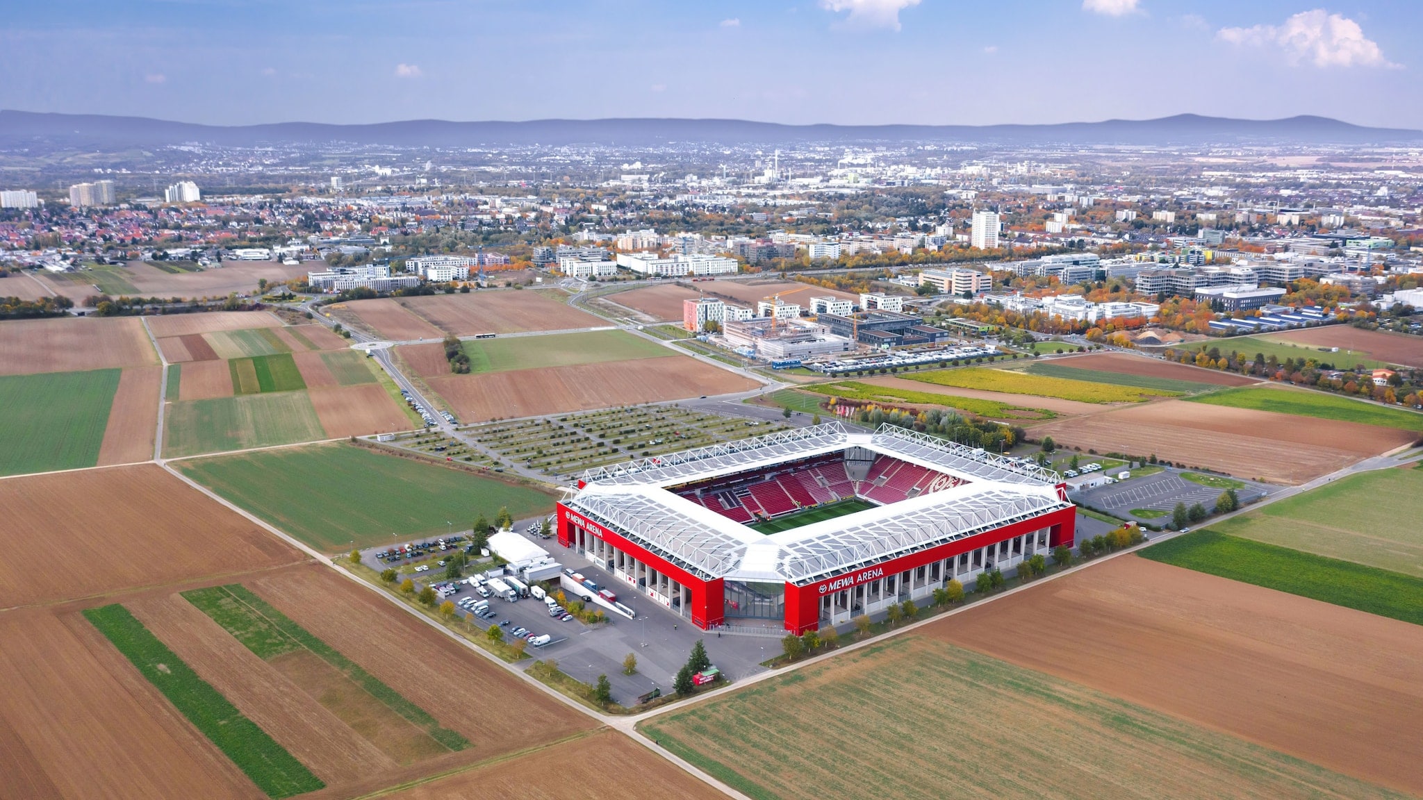 Luftaufnahme von einem rechteckigen Fußballstadion in den Farben Weiß und Rot auf einem Feld am Rande einer Großstadt. Luftaufnahme von einem rechteckigen Fußballstadion in den Farben Weiß und Rot auf einem Feld am Rande einer Großstadt.