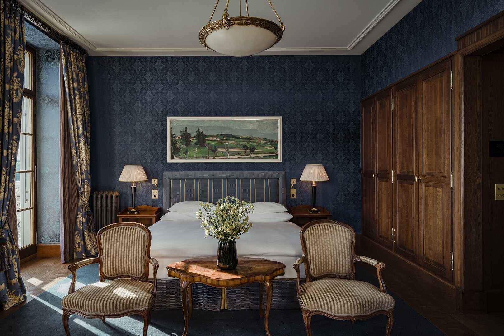 Gemütliches Hotelzimmer mit Doppelbett vor dunkelblauer Tapete und großem Holzkleiderschrank.