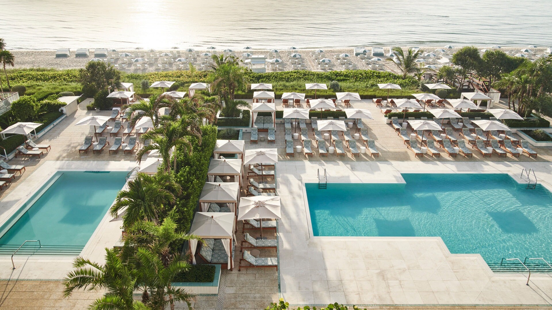 Hotelterrasse mit Palmen und Liegen am Pool an einem weißen Sandstrand mit weiteren Liegen.
