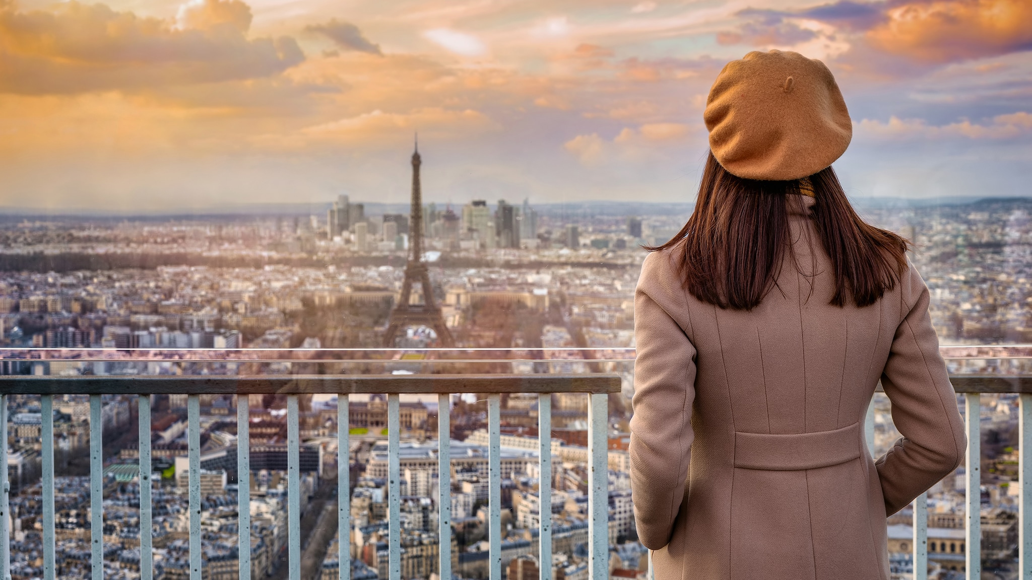 Eine Frau steht vor einem Balkon und guckt auf eine Stadt.