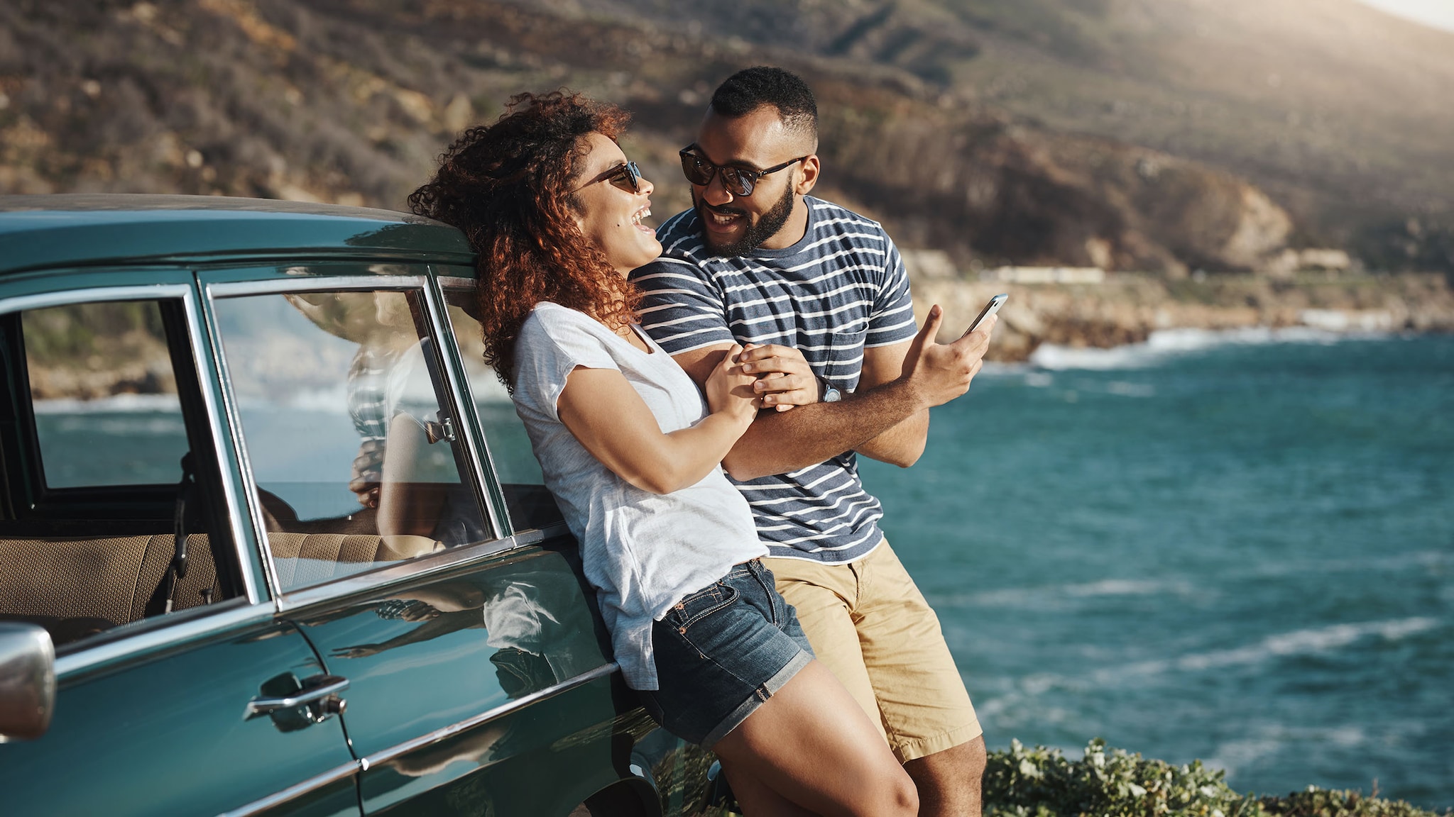 Eine Frau und ein mann lehnen an einem Auto und schauen in die Ferne.