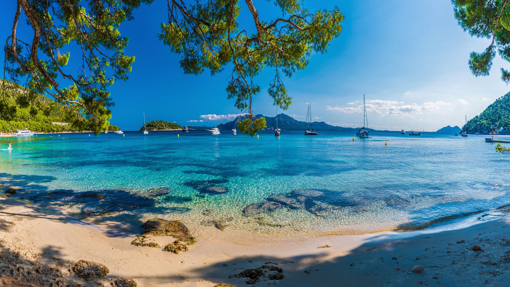 Ein Strand an einem blauen Meer, auf dem Boote schwimmen.