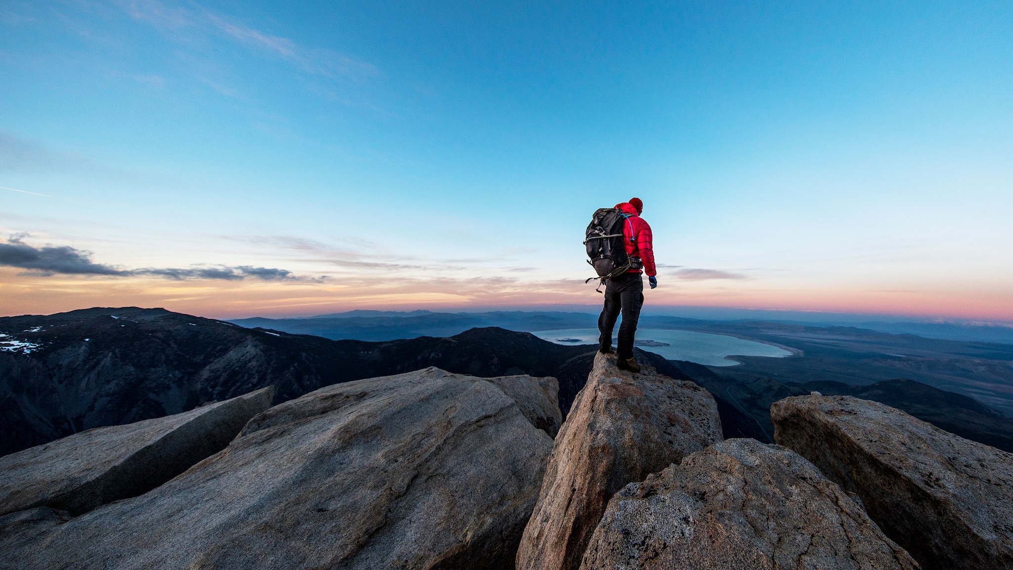 Ein Mann steht auf einem Berg, im Hintergrund geht die Sonne unter.